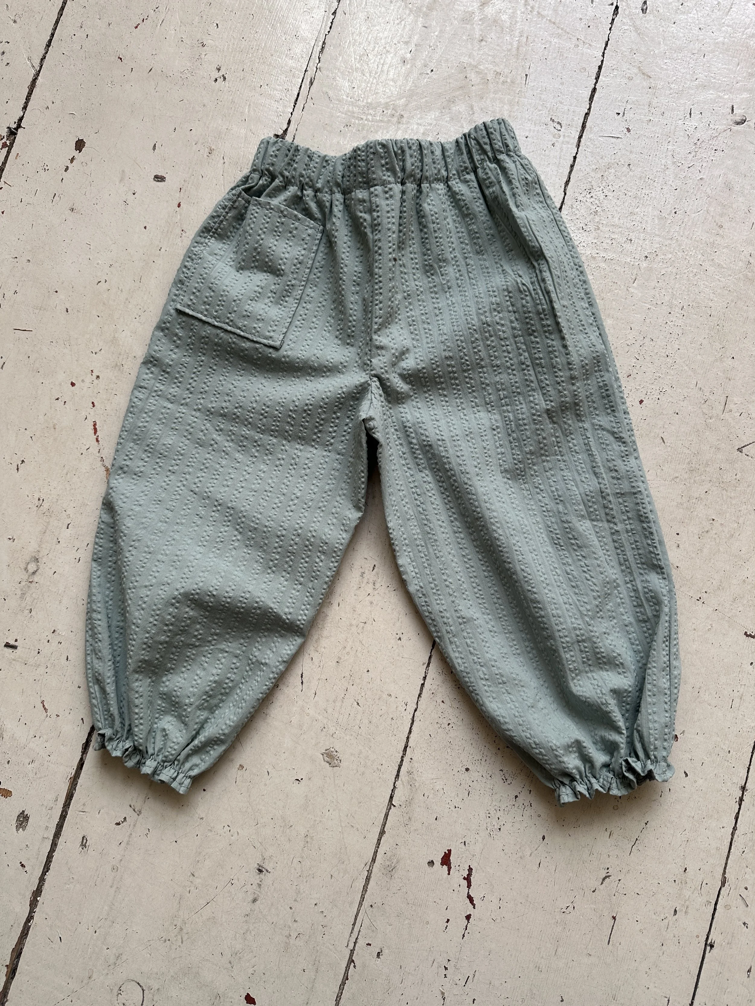 flat lay of organic cotton seersucker barrel trousers duck egg colour, highlight back pocket