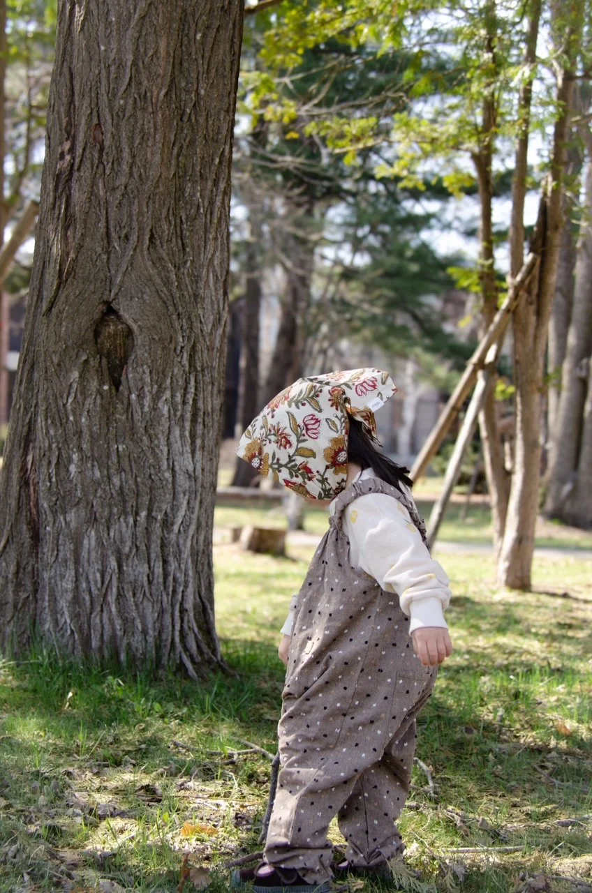 child wearing organic cotton speckled cocoa dungarees, floral handkerchief,