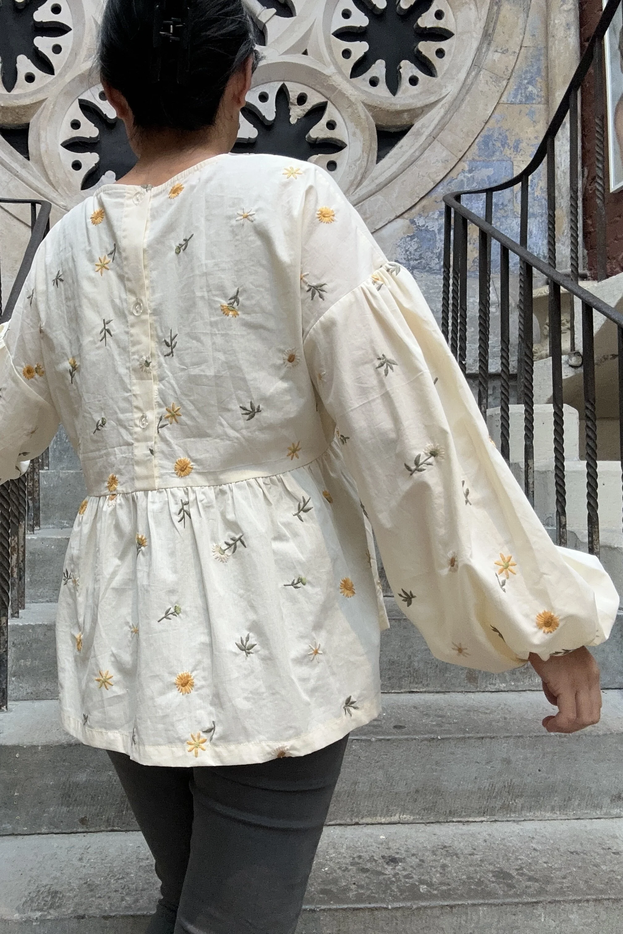 back view of Adult wearing embroidered dandelions Top, Featuring a relaxed fit, balloon sleeves, a statement line of buttons at the back, paired with grey skinny jeans