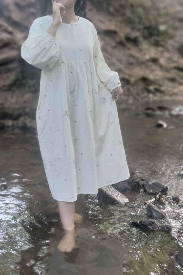 woman wearing while lace flowers embroidered maxi dress walking in a stream in wood