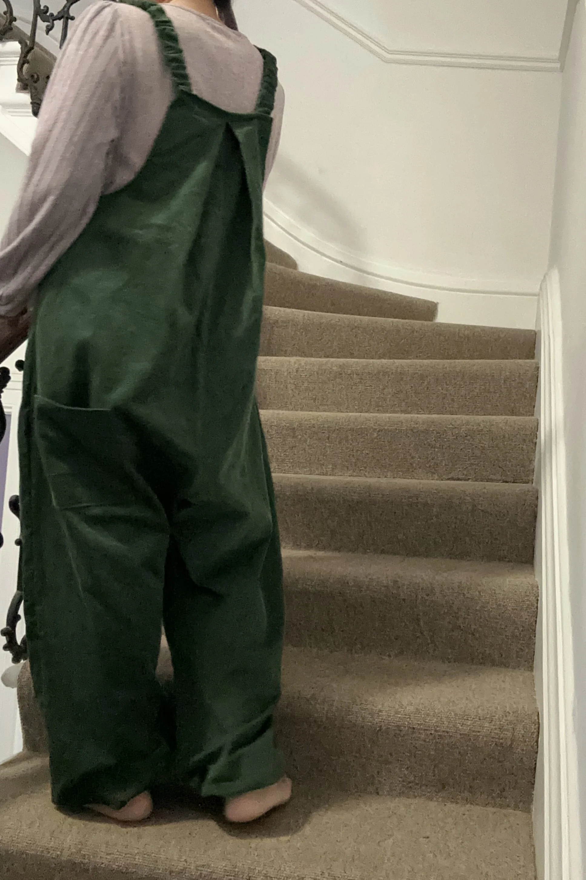 bac view of adult wearing organic cotton needlecord dungarees dark green, layered with lilac top
