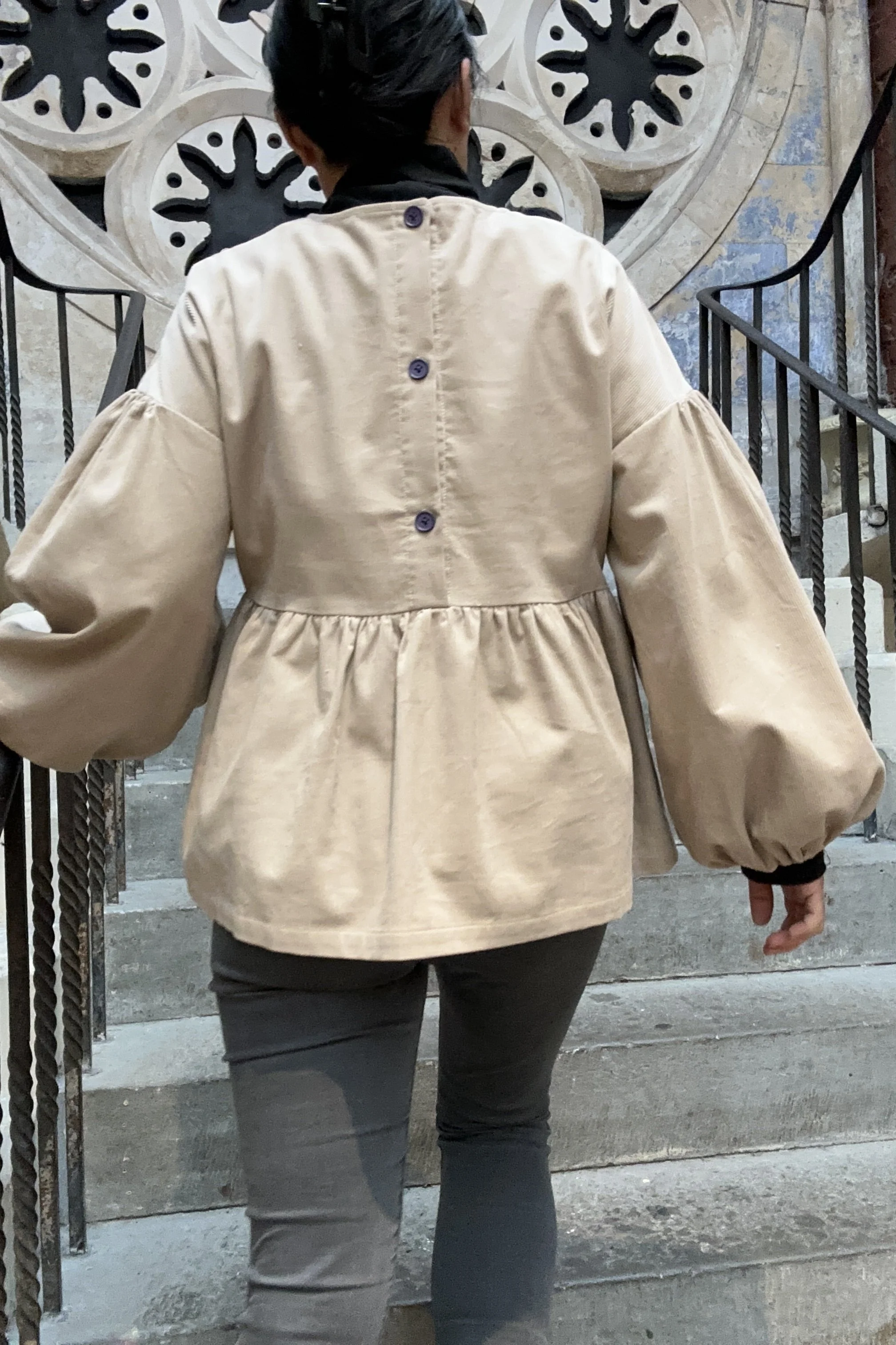 back view of Adult wearing Latte Corduroy Top, Featuring a relaxed fit, balloon sleeves, a statement line of buttons a the back, paired with grey skinny jeans