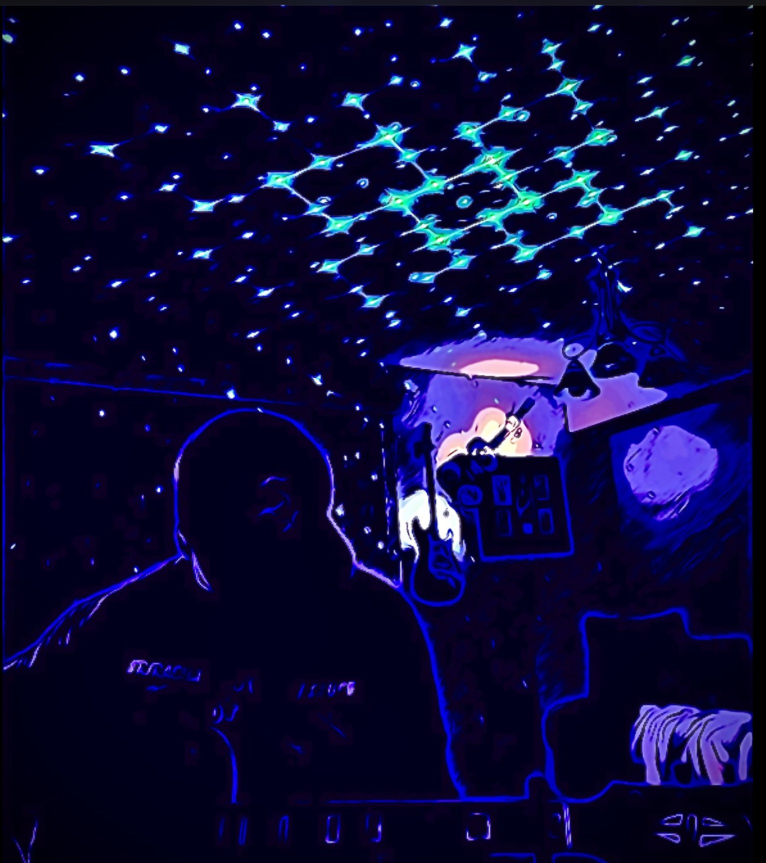 A person is sitting at a table under a ceiling decorated with blue star-shaped lights. The person's silhouette is outlined in neon. There are objects on the table, including a deck of cards, a cube-shaped object with digital displays, and a small animal figurine. The room has dark walls, creating a glowing, cosmic atmosphere.