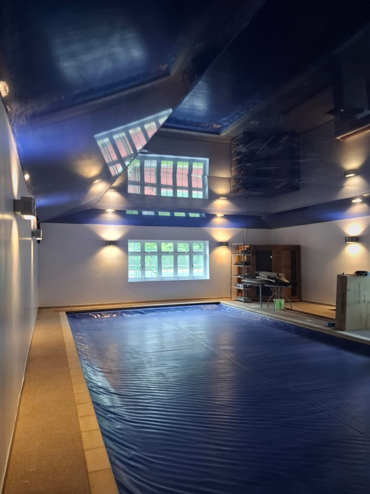 Indoor pool with blue cover, large windows, and wooden furniture in a well-lit room.