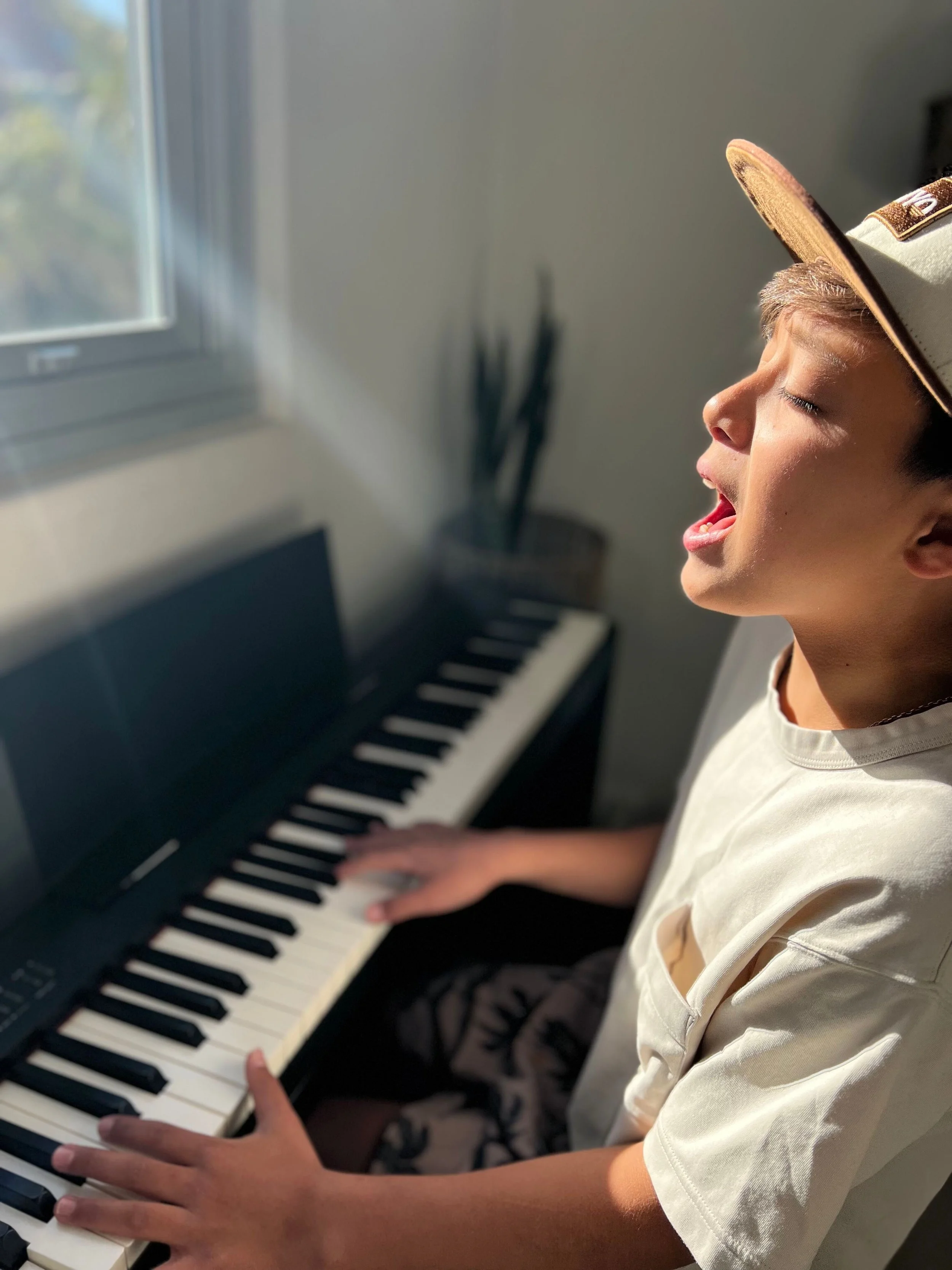 Taiyo Marchand, A boy singing passionately while playing a digital piano in a sunlit room.