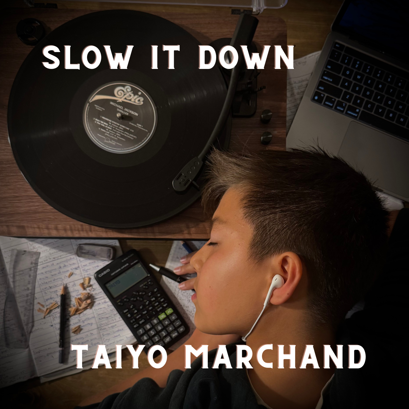 Taiyo, a young man with short hair and white earphones sleeping at a cluttered desk with pencils, a calculator, notebooks, a pen, a laptop, and a vinyl record player. Text overlay says 'Slow It Down' and 'Taiyo Marchand' as the cover of a song.
