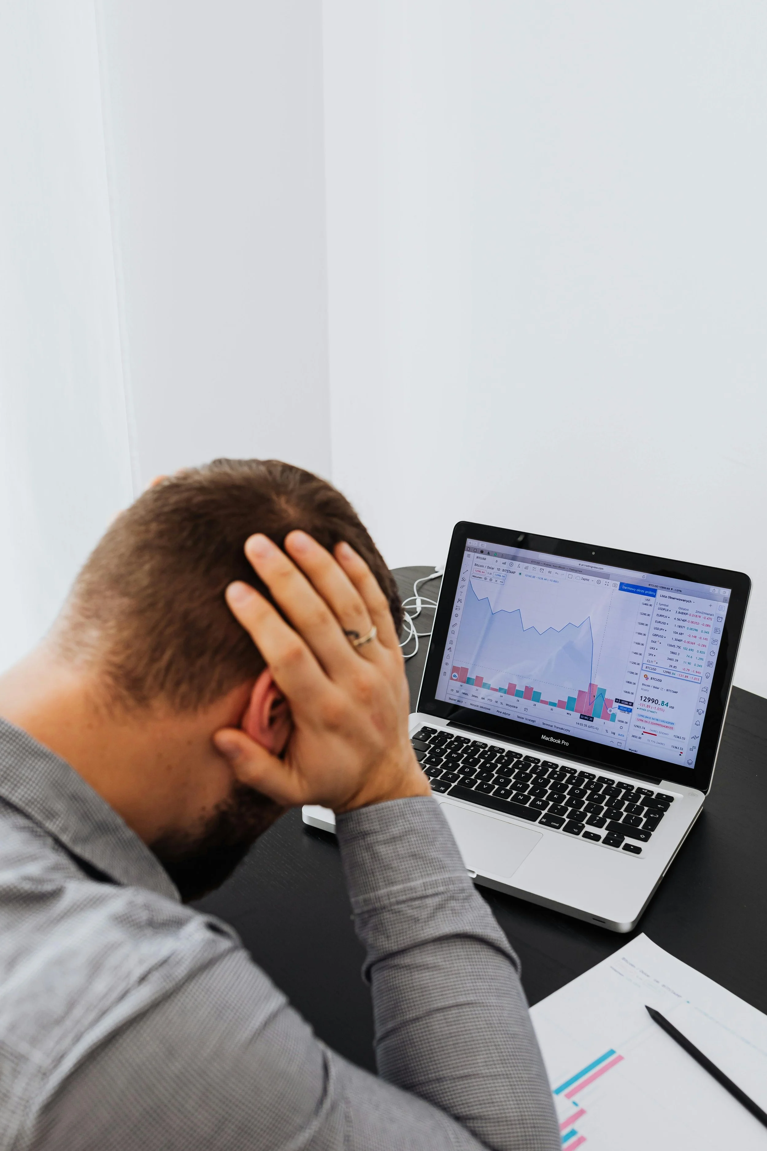 Man with head in hands looking at a laptop screen displaying stock or financial charts and graphs.