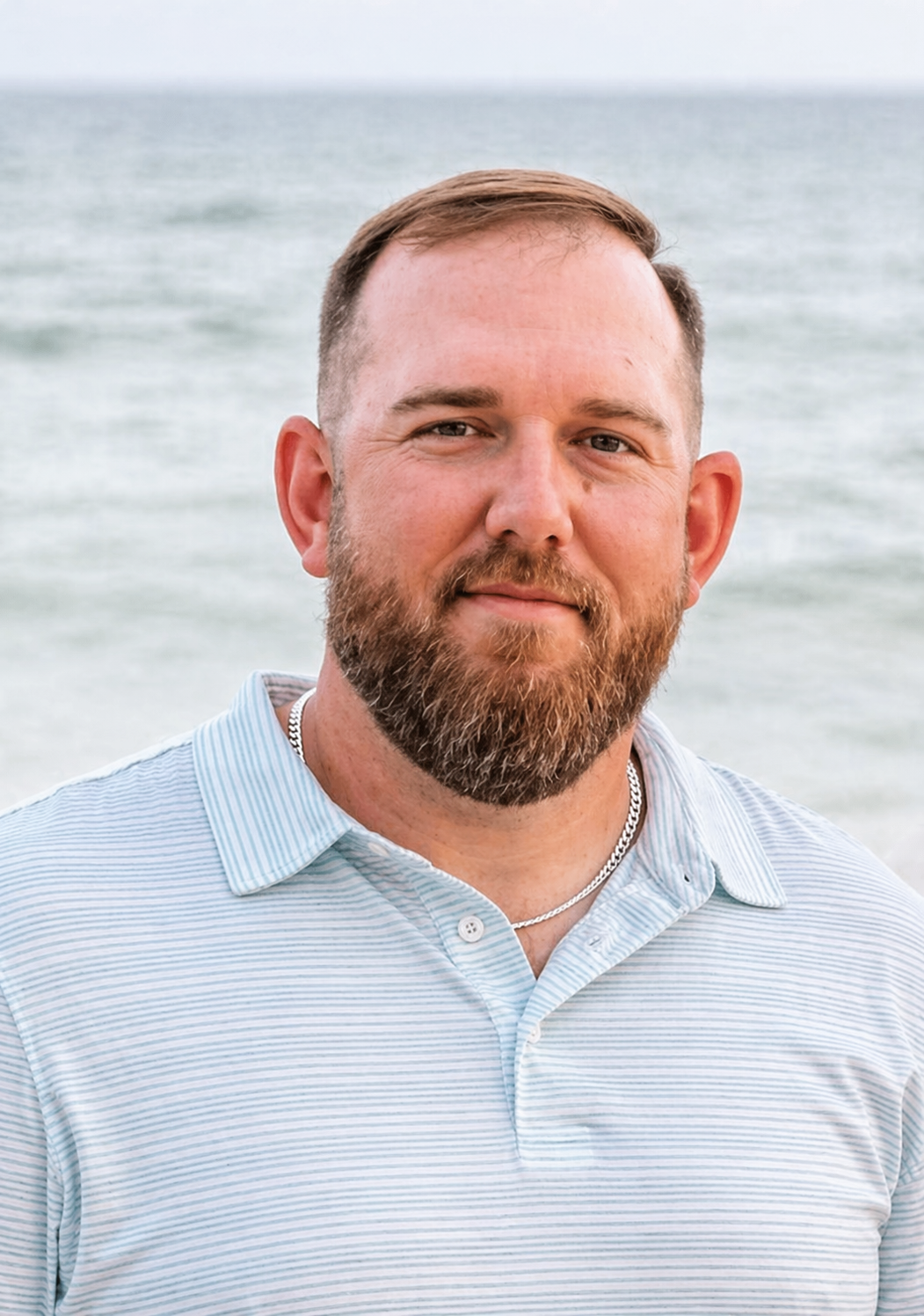 Portrait of a man with a beard and mustache smiling in front of a body of water.