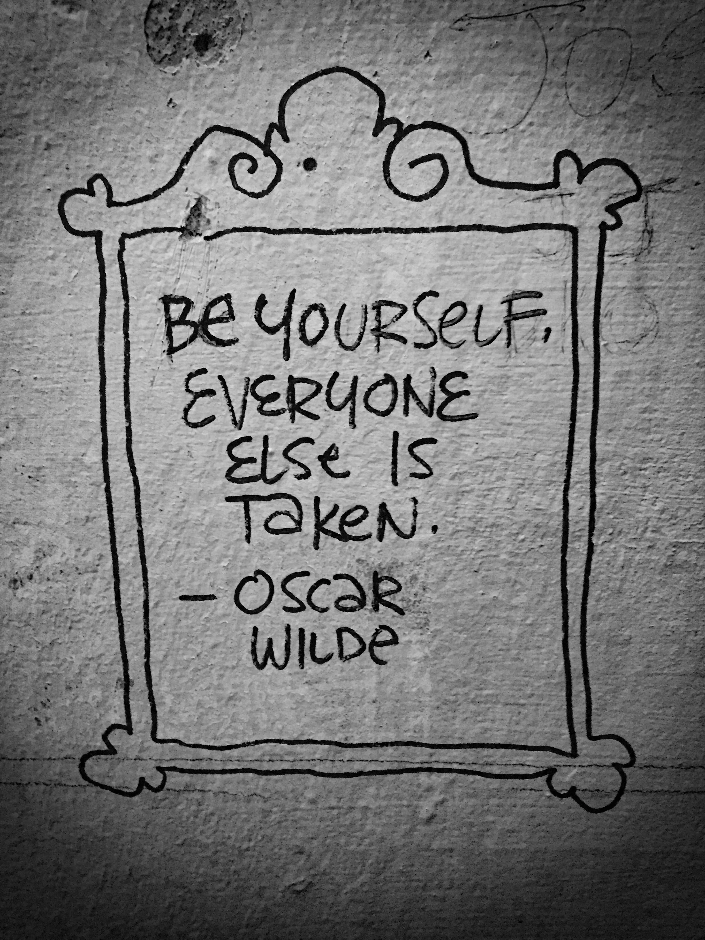 A hand-drawn quote on a wall that reads, 'Be yourself, everyone else is taken. - Oscar Wilde,' surrounded by a decorative frame.