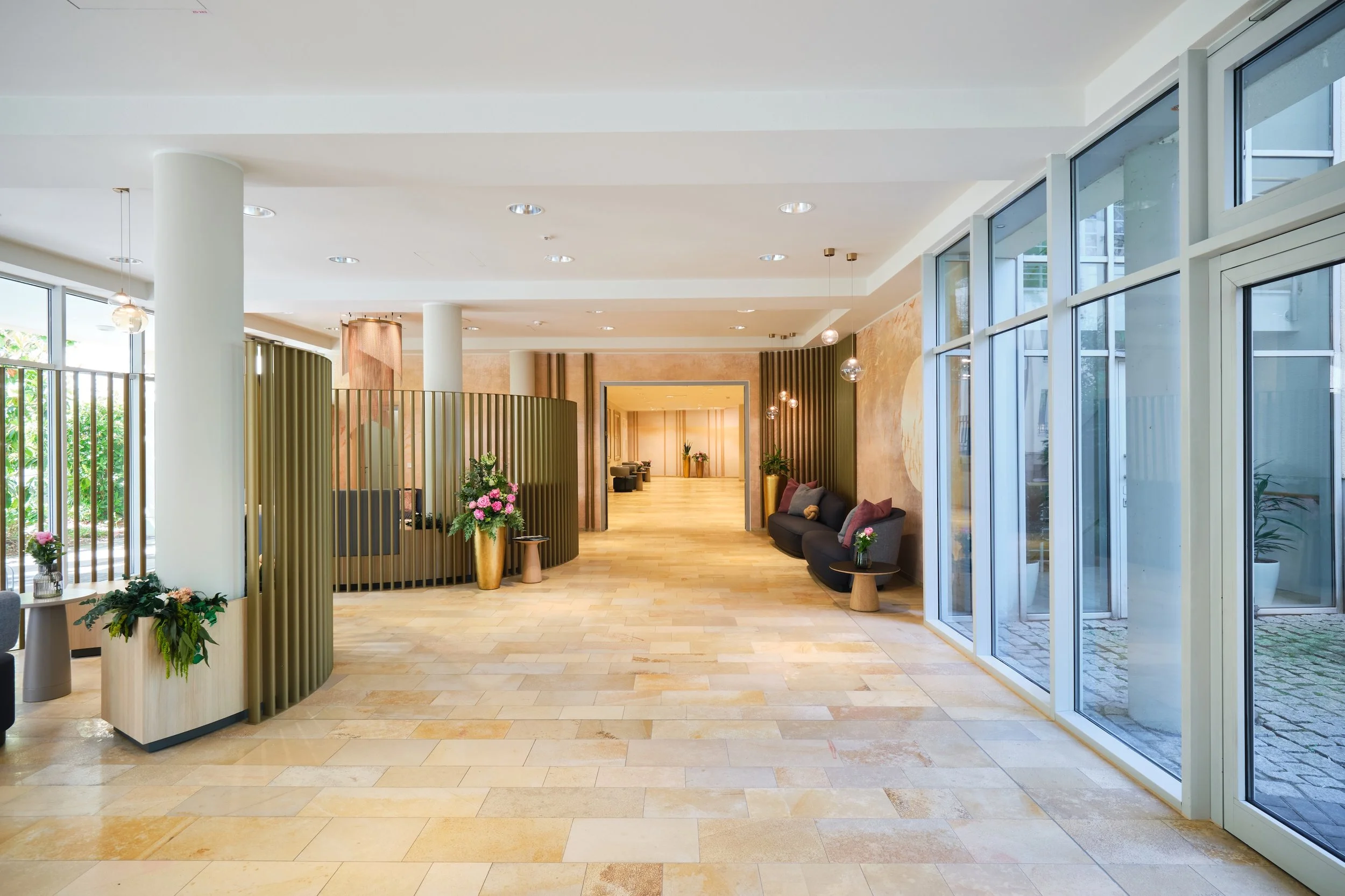 Moderne, helle Hotellobby mit großen Fensterflächen, Sitzgelegenheiten, Pflanzen und Dekorationen.