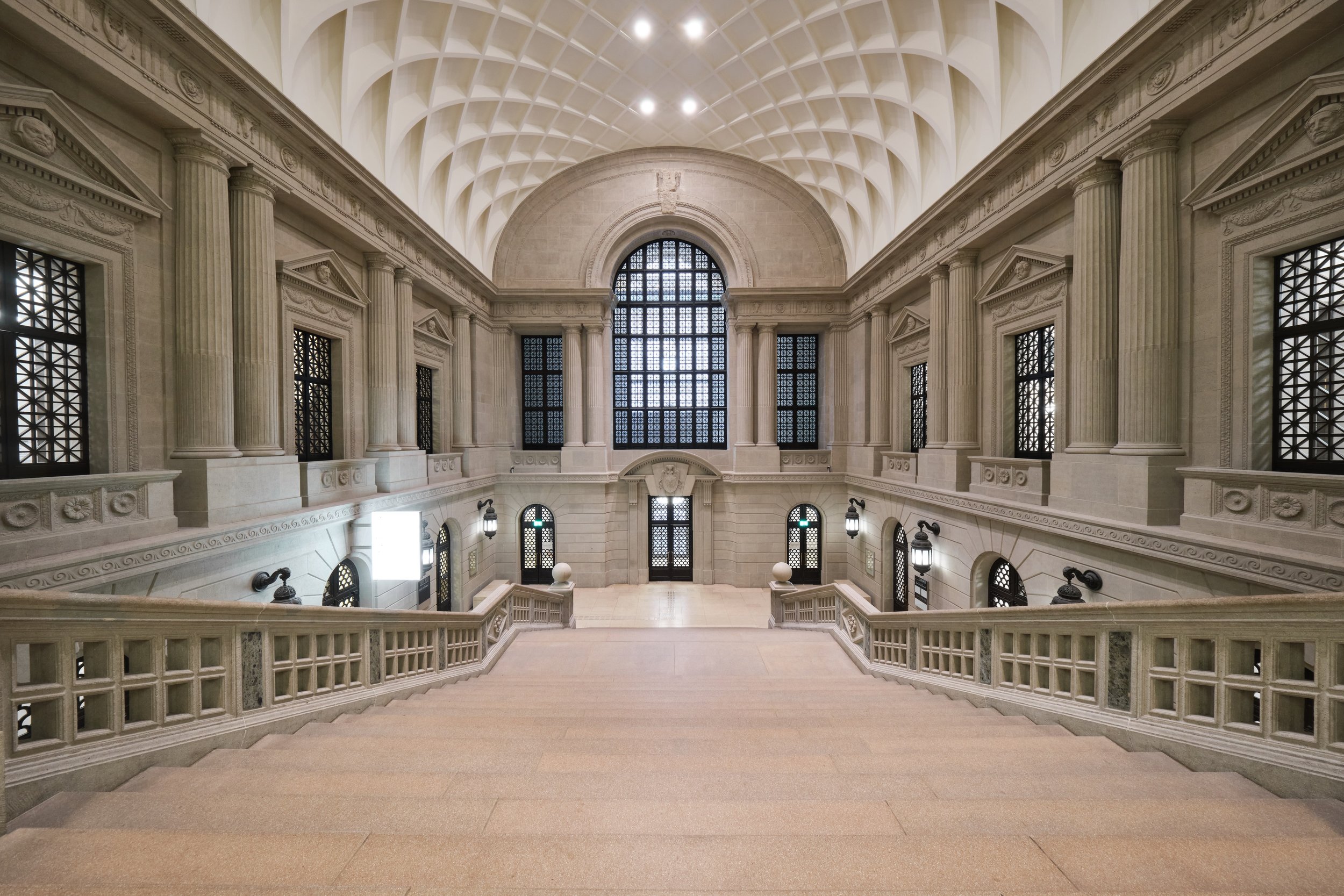 Innenaufnahme eines prächtigen, historischen Gebäudes mit hohen Bögen, großen Fenstern und klassischen Säulen, Treppen führen zu einer oberen Galerie.