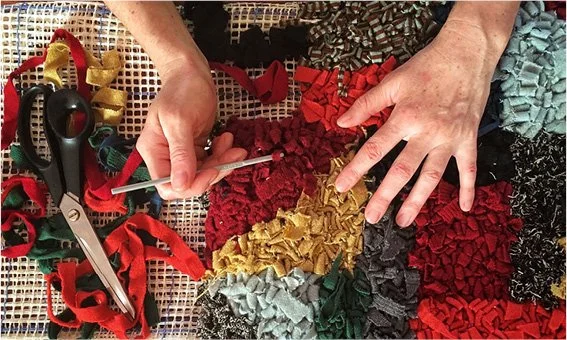 Hands working on fabric pieces with scissors and sewing tools, surrounded by various colorful fabric scraps.