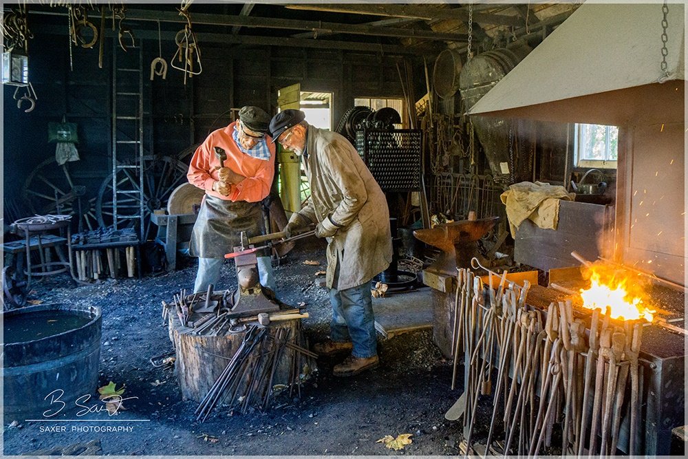 Two blacksmiths working in a traditional workshop with tools and a fire furnace.