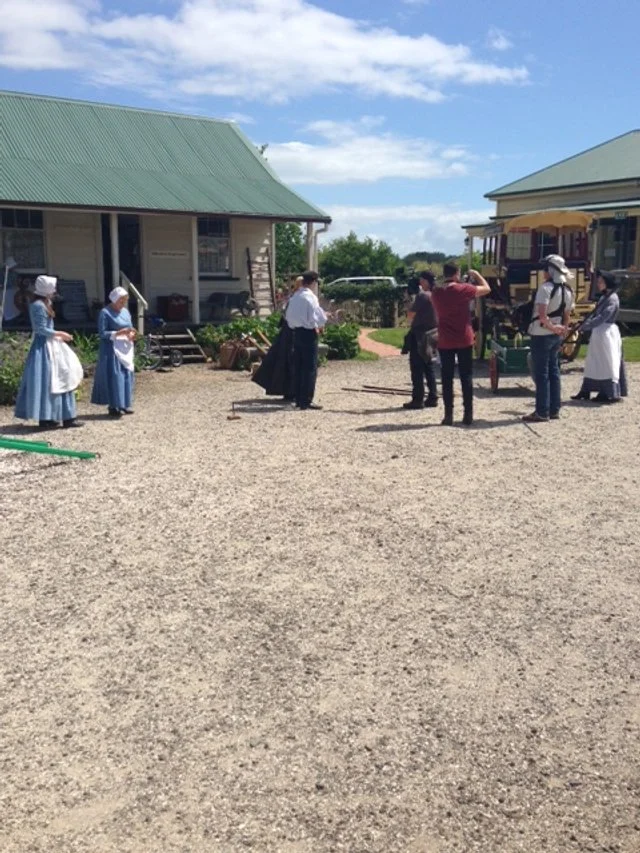 People dressed in 19th-century clothing standing outside near a vintage train on a sunny day.