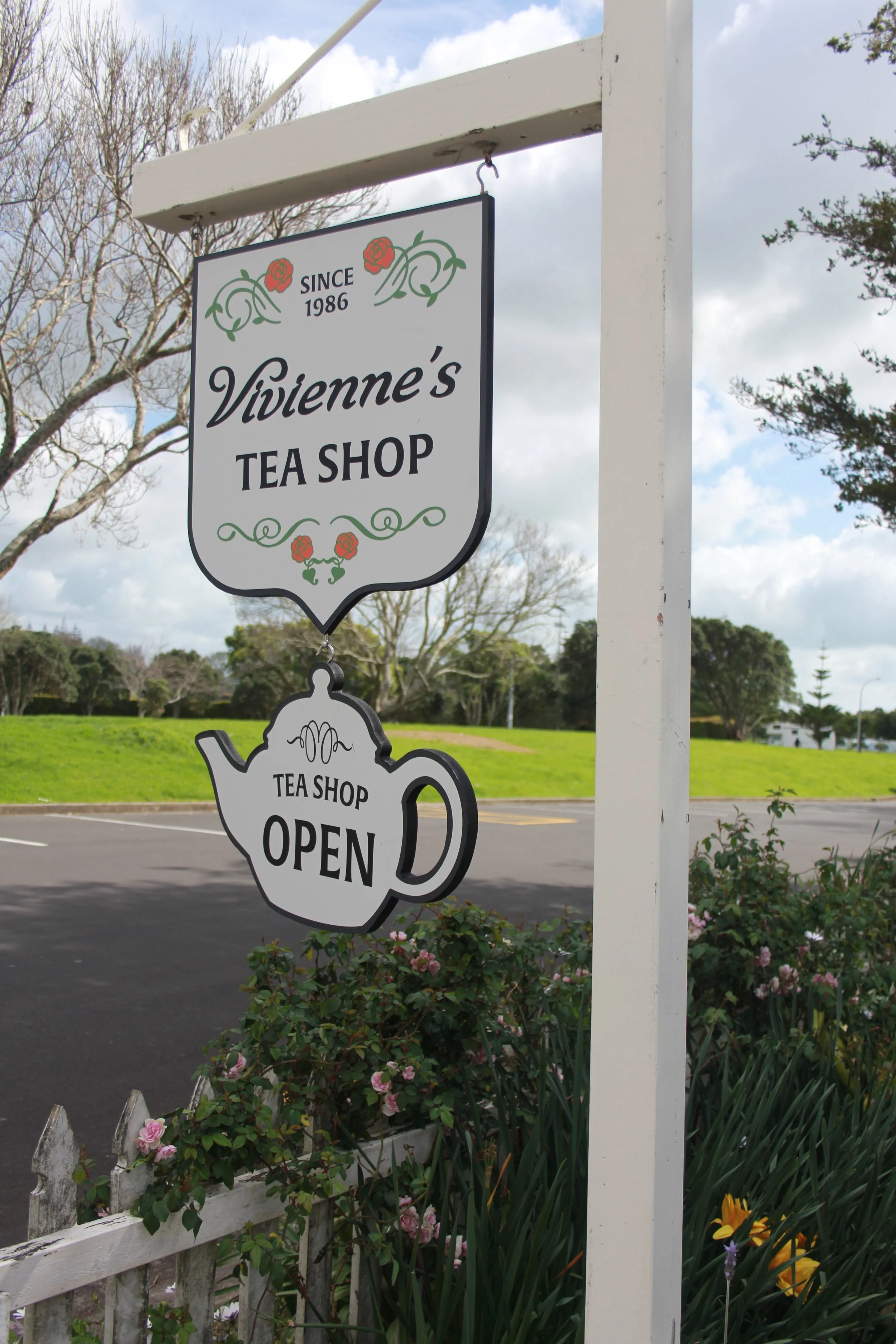 Sign for Vivienne's Tea Shop, established in 1986, with a decorative flower and vine design, featuring an attached cutout of a tea pot that says 'Tea Shop Open'.
