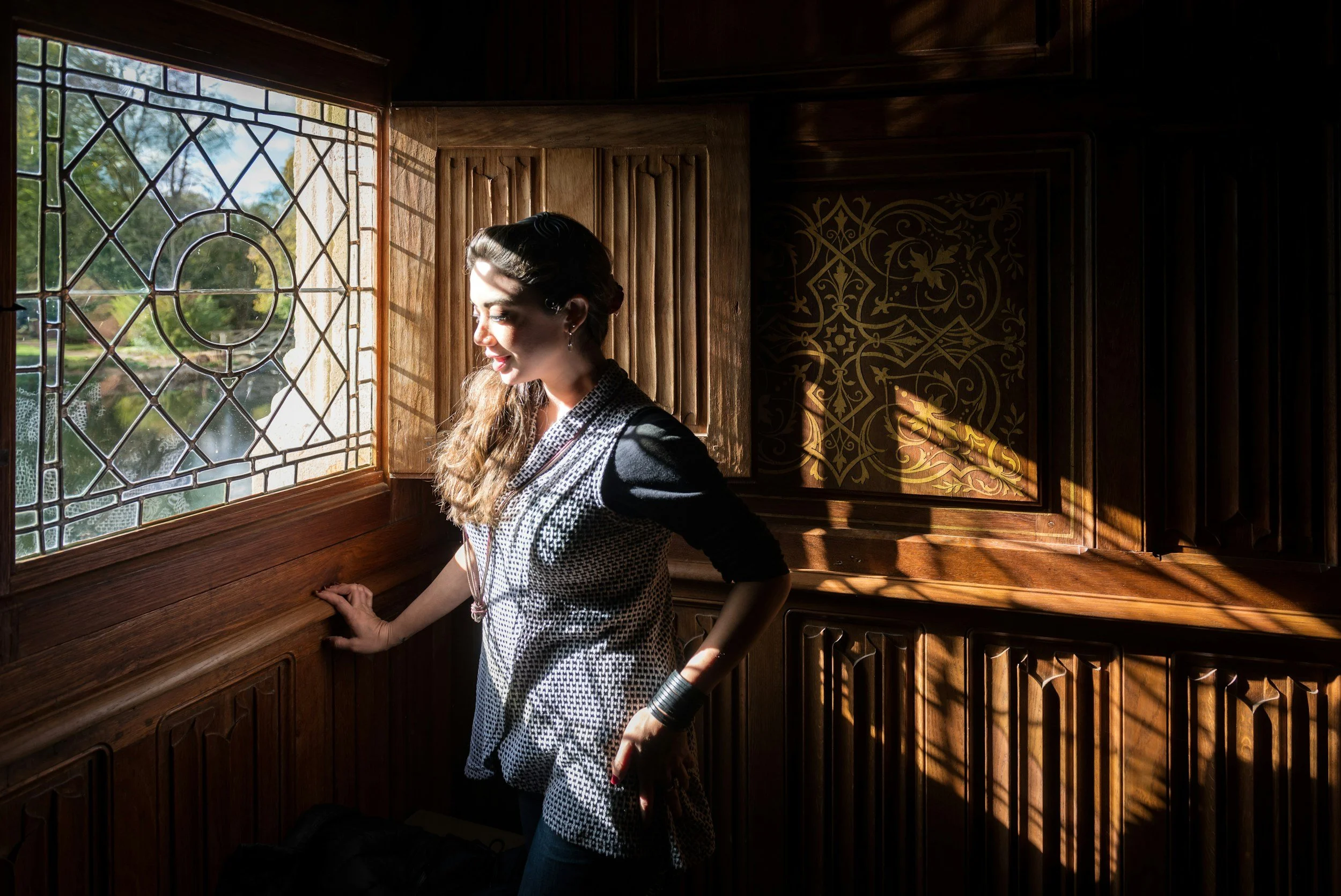 A woman smiling in sunlight by a stained-glass window, representing the emotional lightness and reconnection found through somatic Mind-Body Bowen therapy.