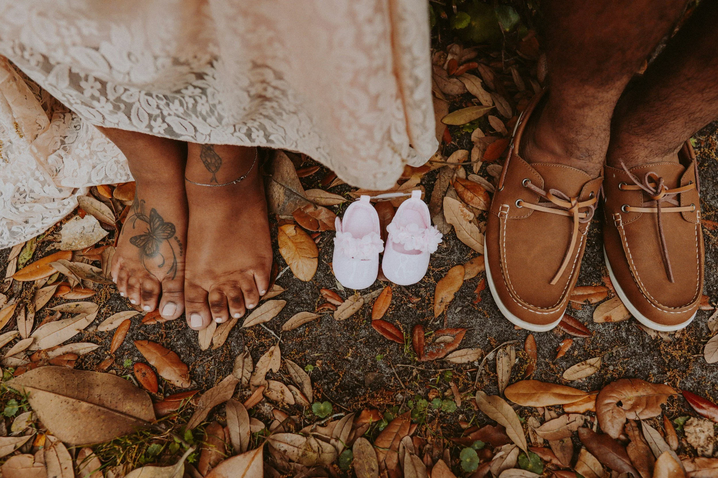 A symbolic overhead shot of an adult man and woman's feet next to a pair of tiny baby shoes, representing the journey of matrescence and the intentional creation of a birth circle.