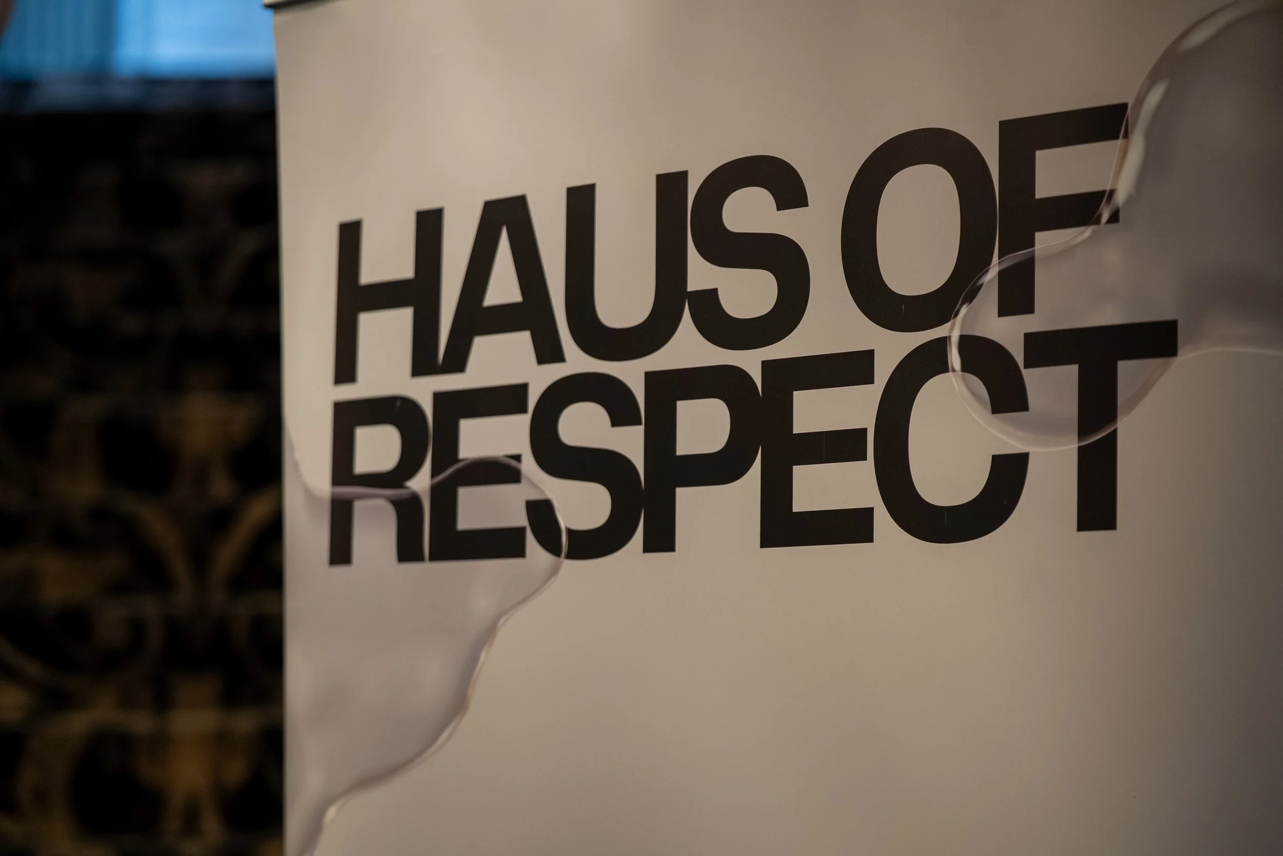 A white paper bag with bold black text that reads 'Hause of Respect'. The bag is held by a person, with a balloon string visible near the bottom of the image. The background appears to be a dark, textured surface.