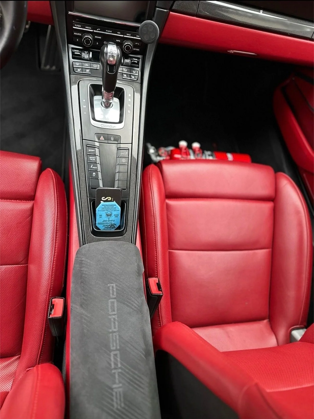 Inside a luxury car with red leather seats, visible gear shifter and center console with controls, and fire extinguishers in the passenger footwell.
