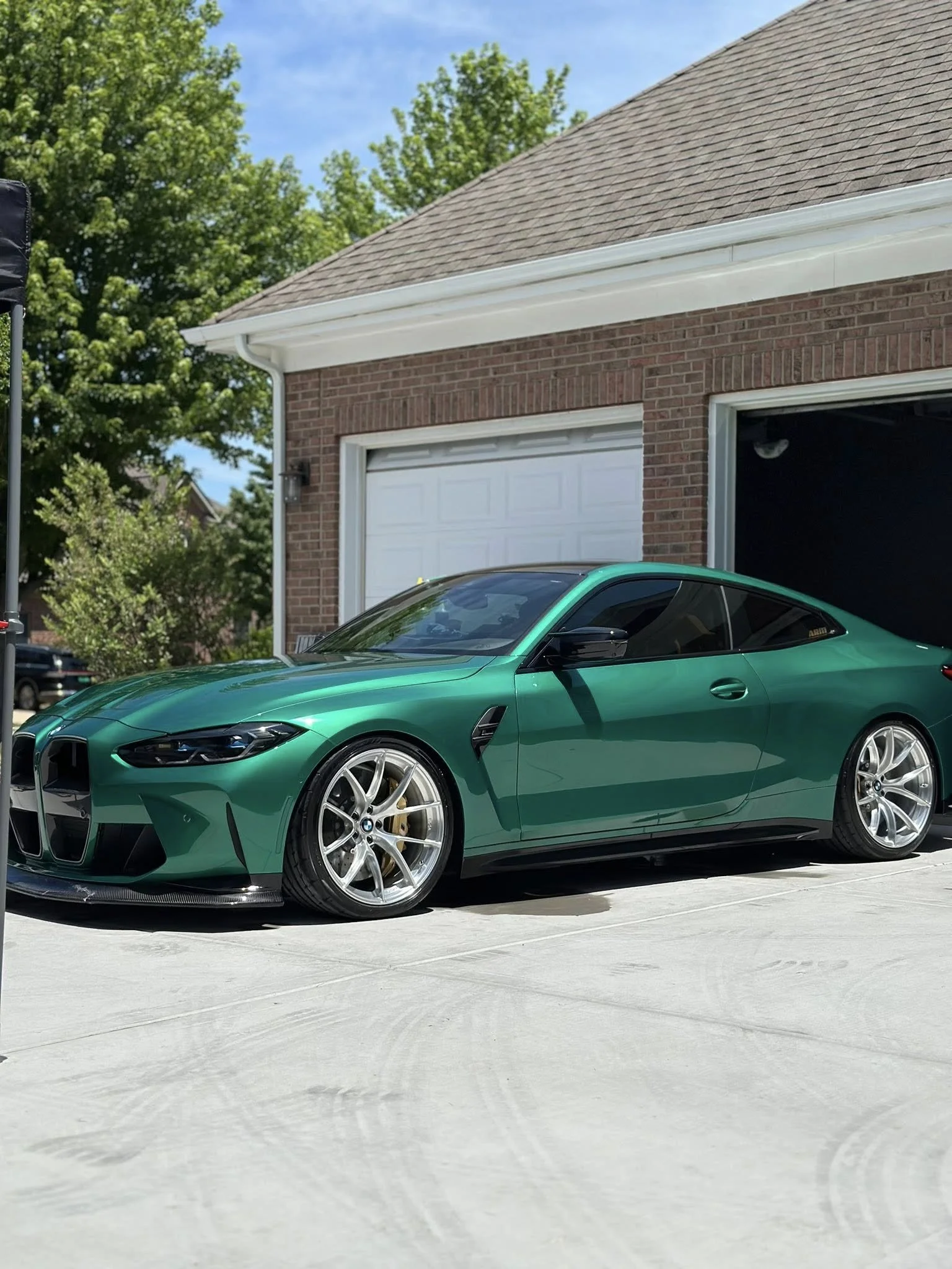 A green sports car parked in a residential driveway next to a brick house with a white garage door.