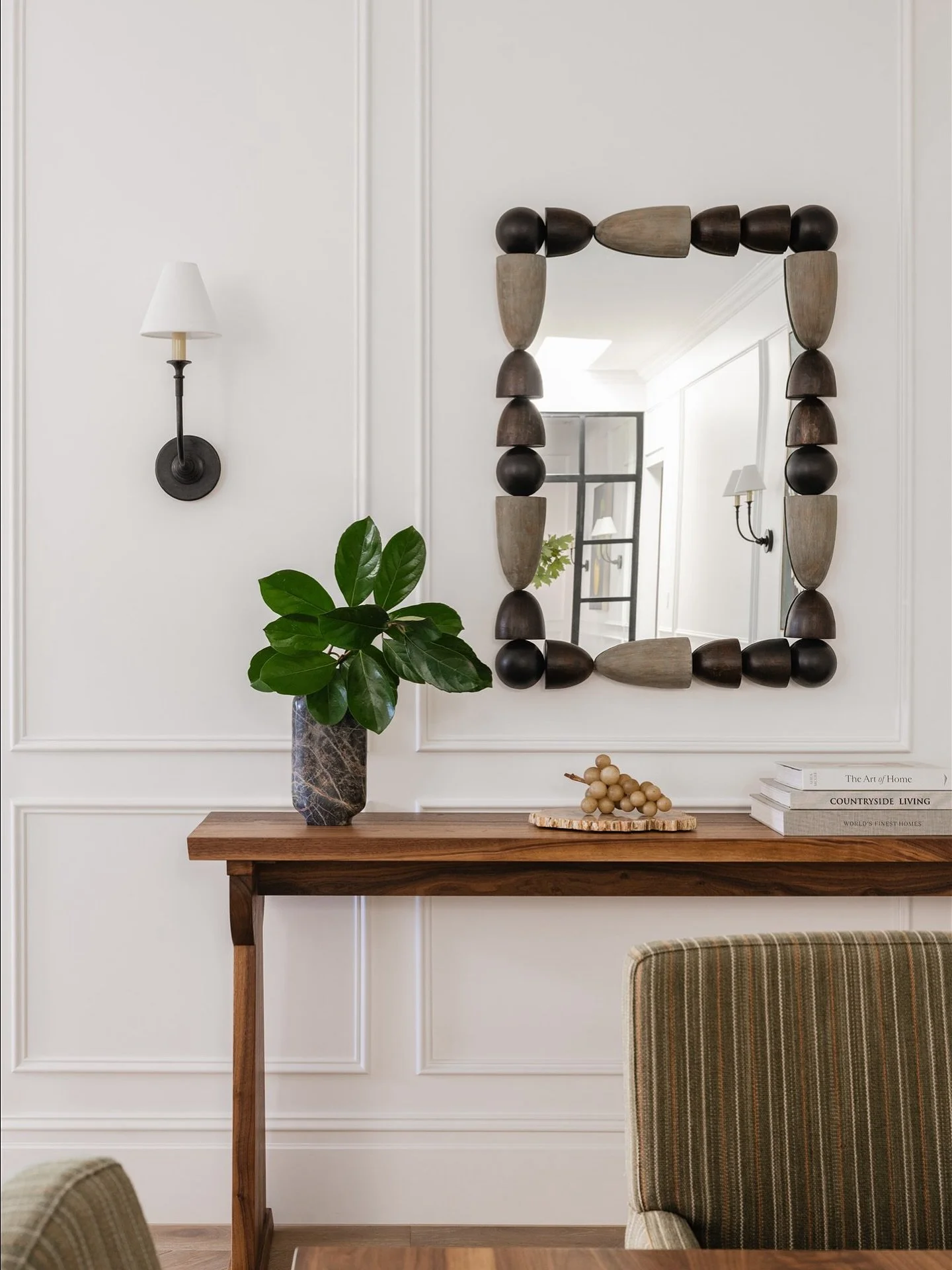 A glimpse into the dining space beyond the entry.
Wall panelling continues seamlessly, framing a sculptural mirror, custom console and aged iron sconces. Verde marble, alabaster grapes, and collected details offer a hint of the open-plan living beyon