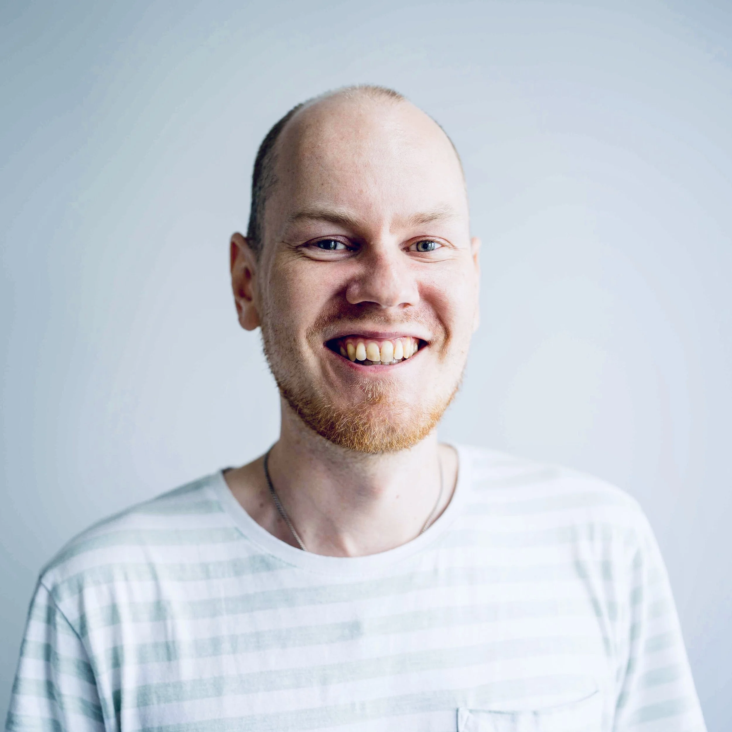 The person is smiling in a white and grey and white striped T-shirt on a white background.