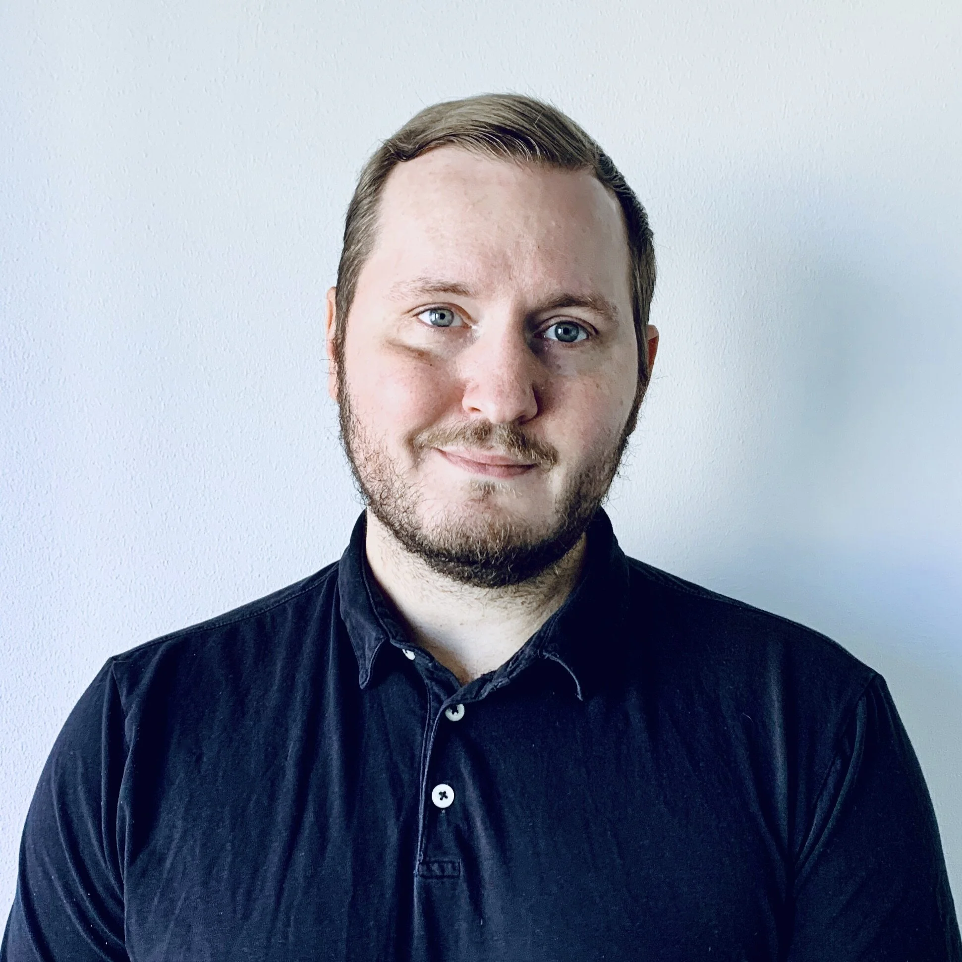 A person is standing on a white background, looking at the camera and smiling.