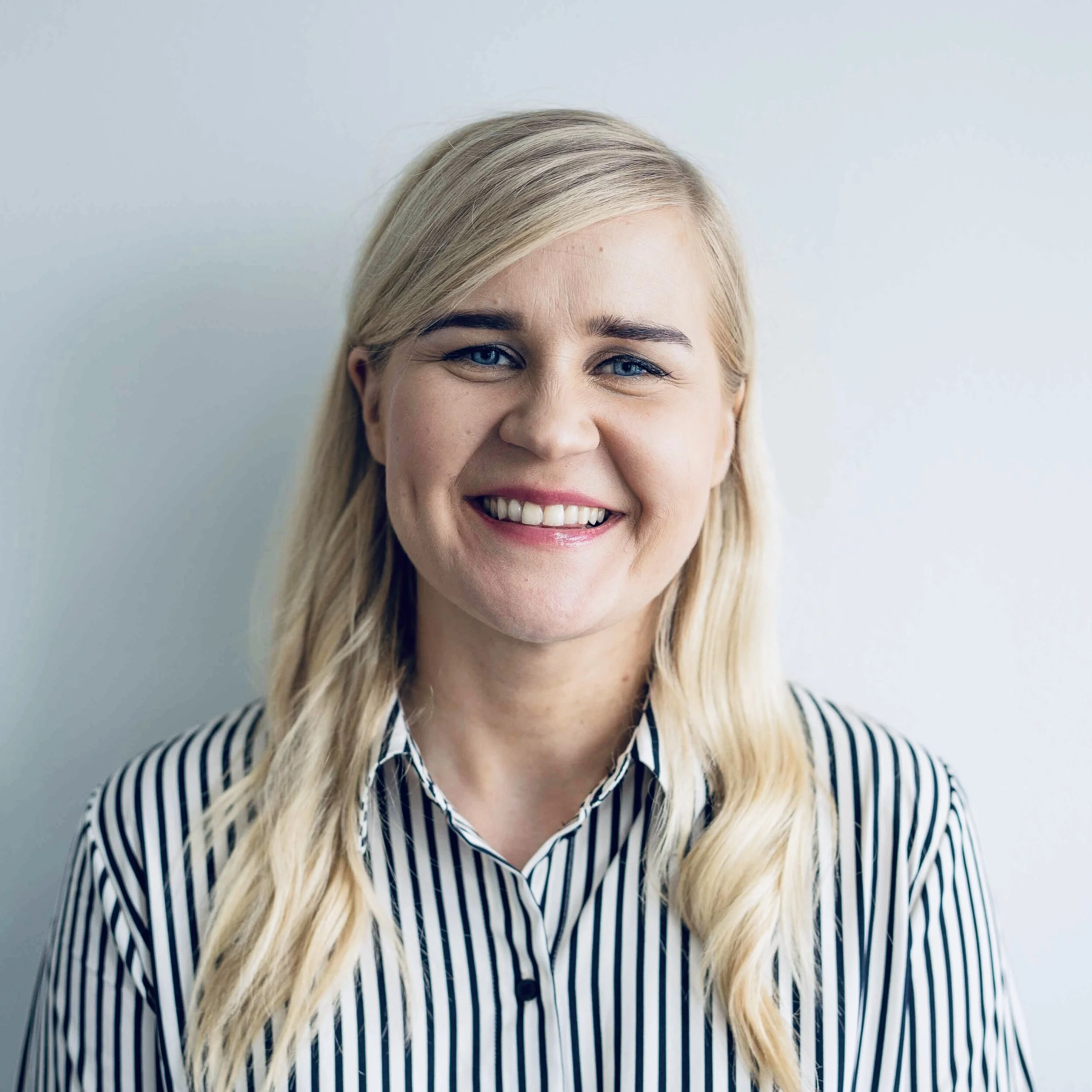 Smiling woman, blonde long hair and striped shirt, neutral background.