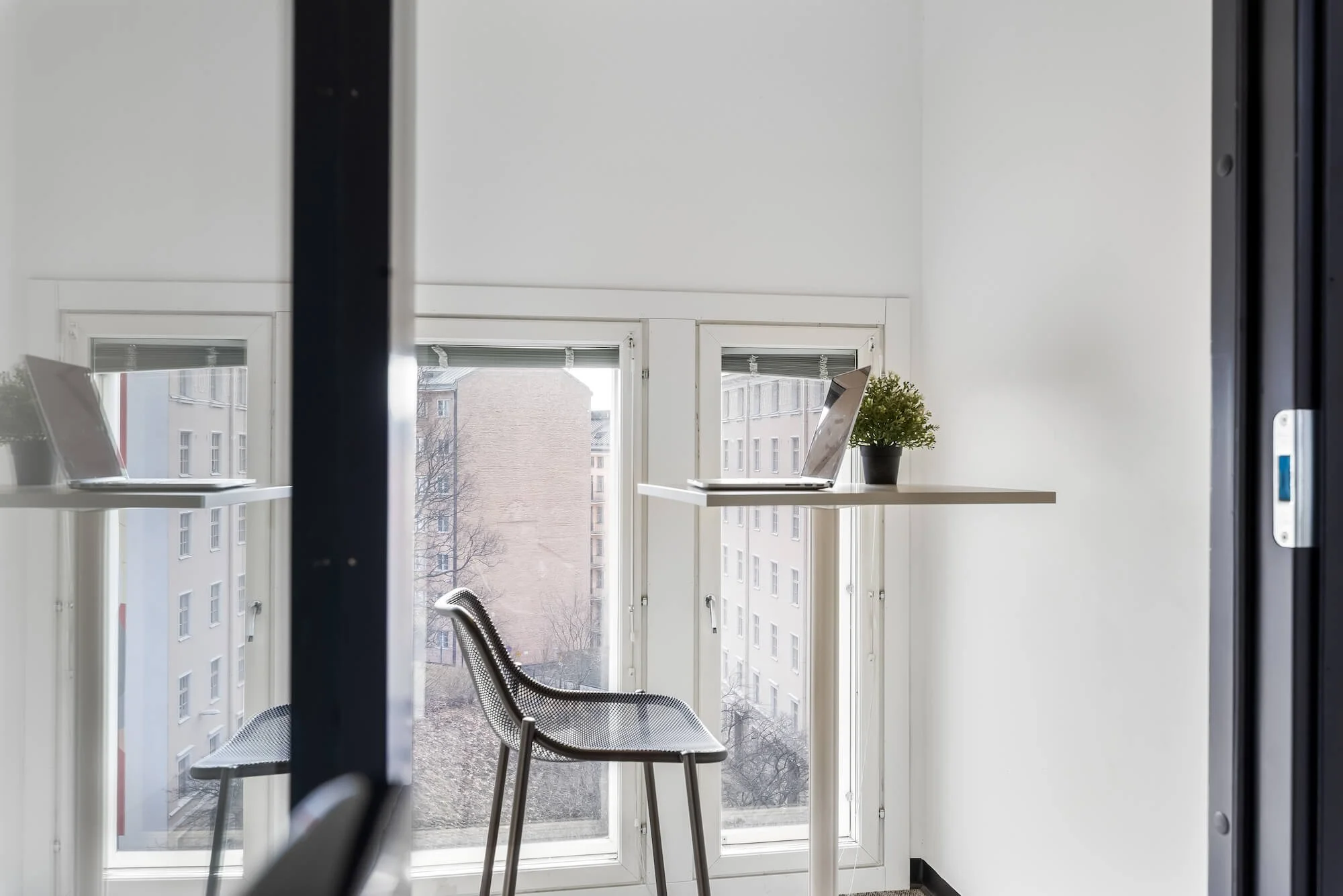 An empty, modern call center with floor-to-ceiling windows, a wooden table and chairs, gray furniture, and a houseplant, featuring a bright and minimalist look.