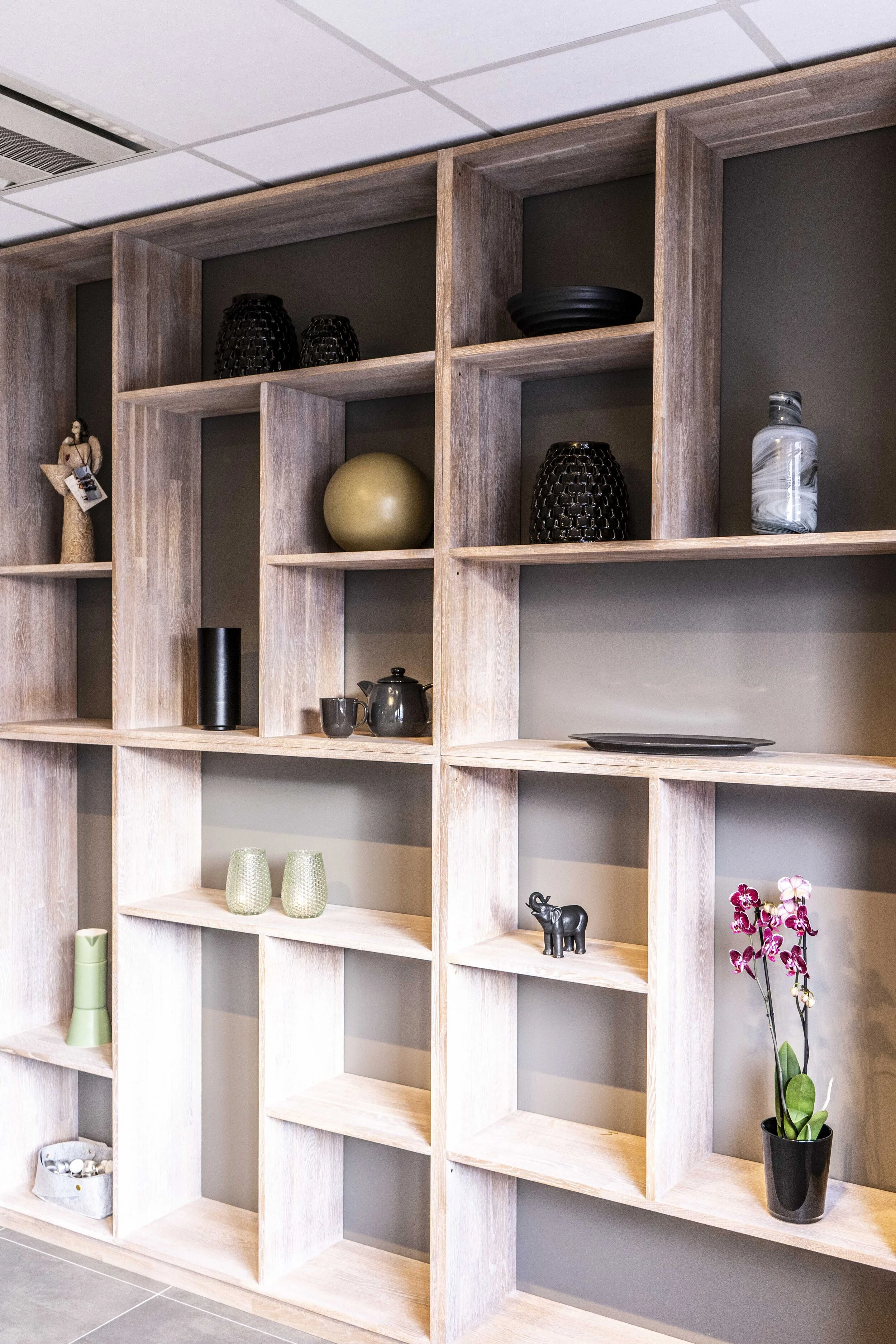 Vegghylle med dekorative gjenstander, inkludert keramikk, planter og pynteting.