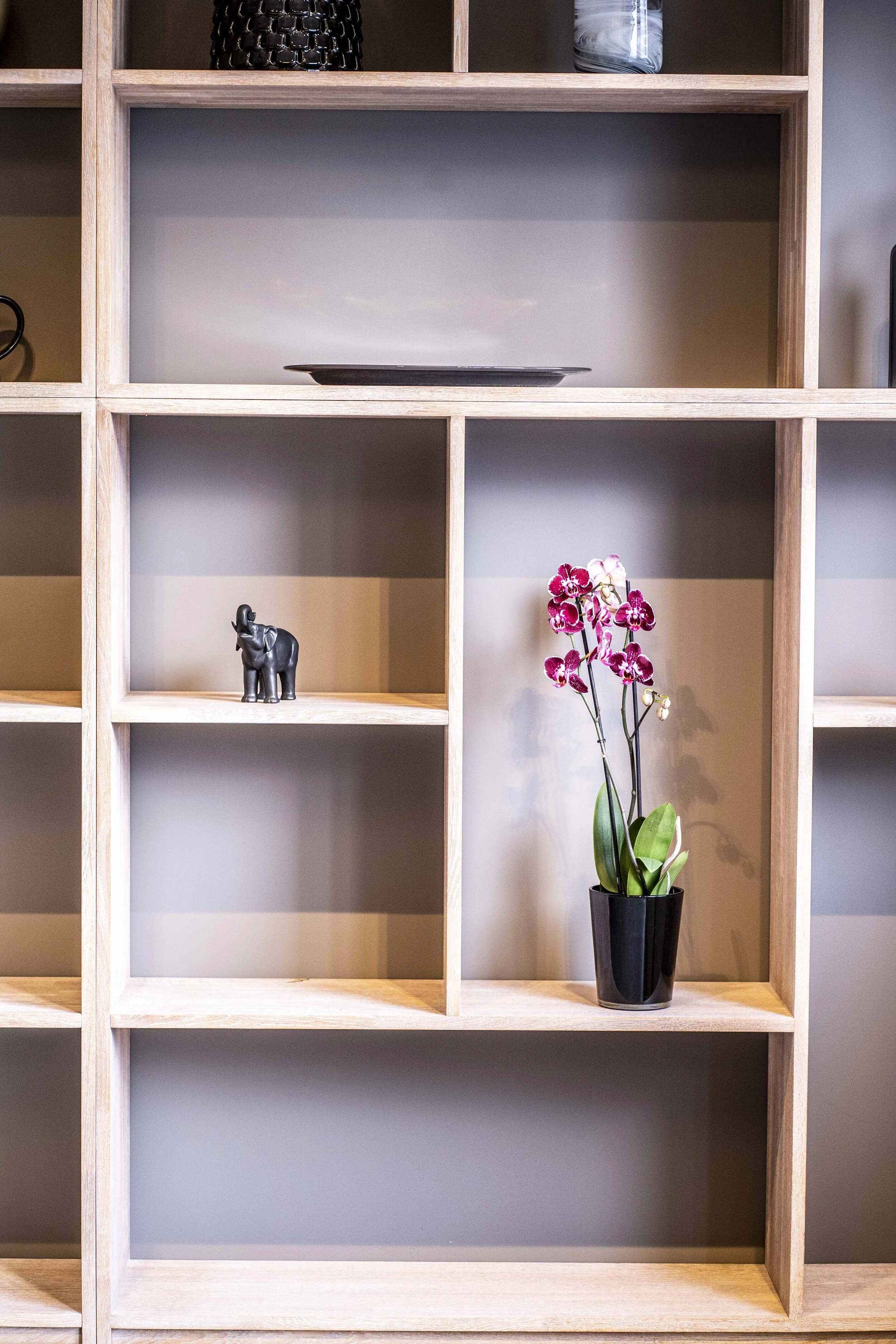 Trehylle med dekorative gjenstander, inkludert en svart elefantfigur, en tallerken og en potteplante med lilla blomster.