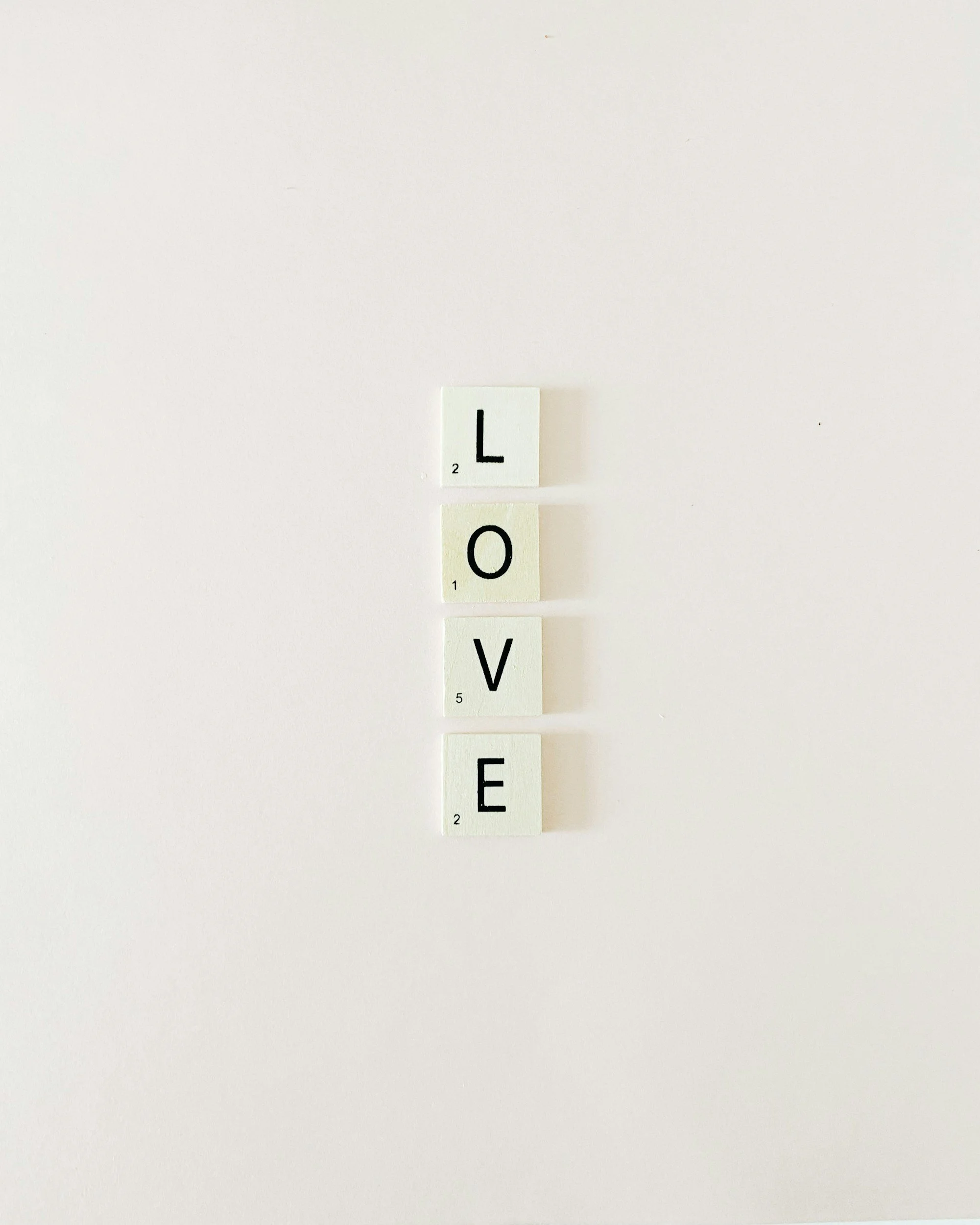 Four Scrabble tiles spelling 'LOVE' on a white background.
