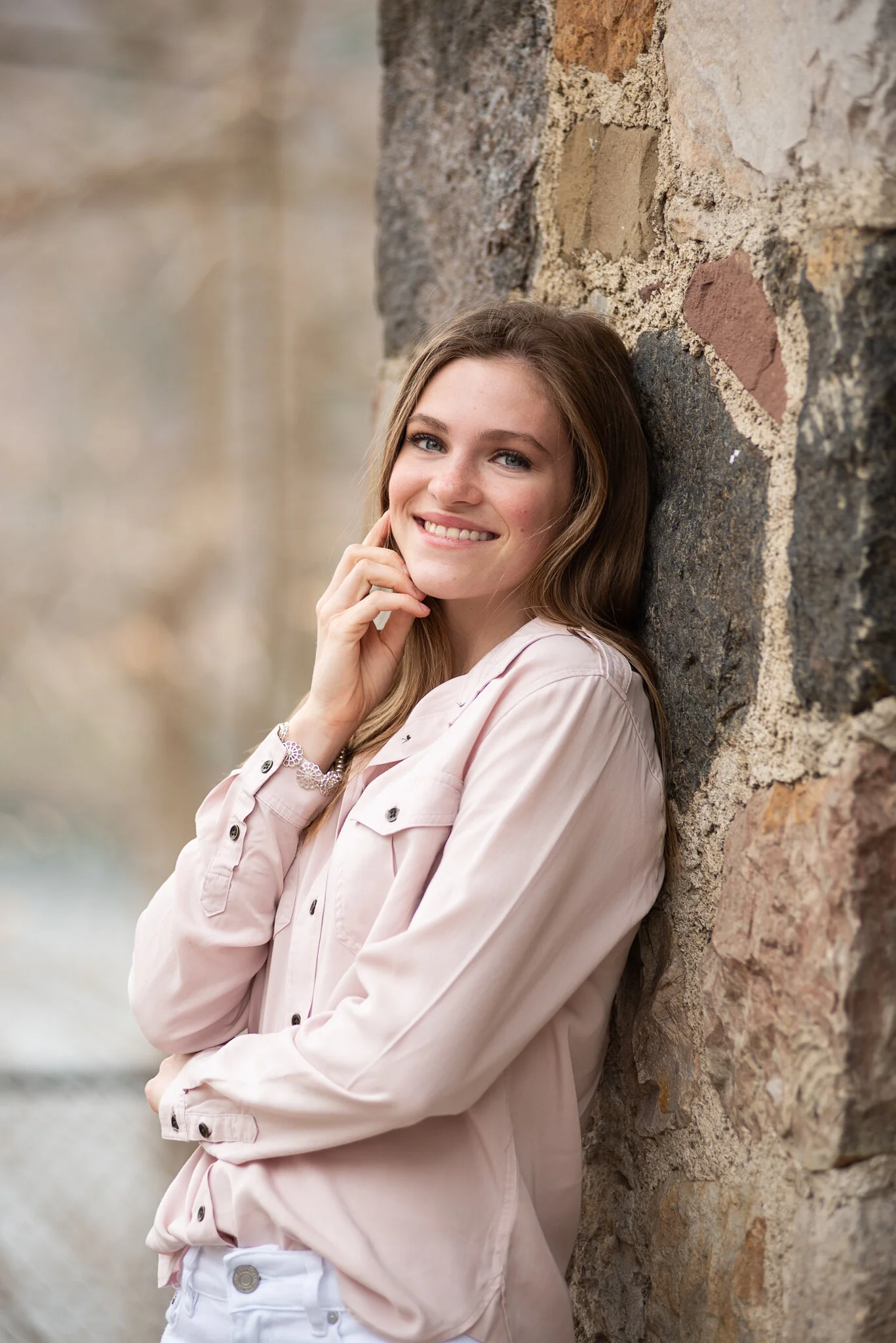senior in soft neutral colors posing against a stone wall