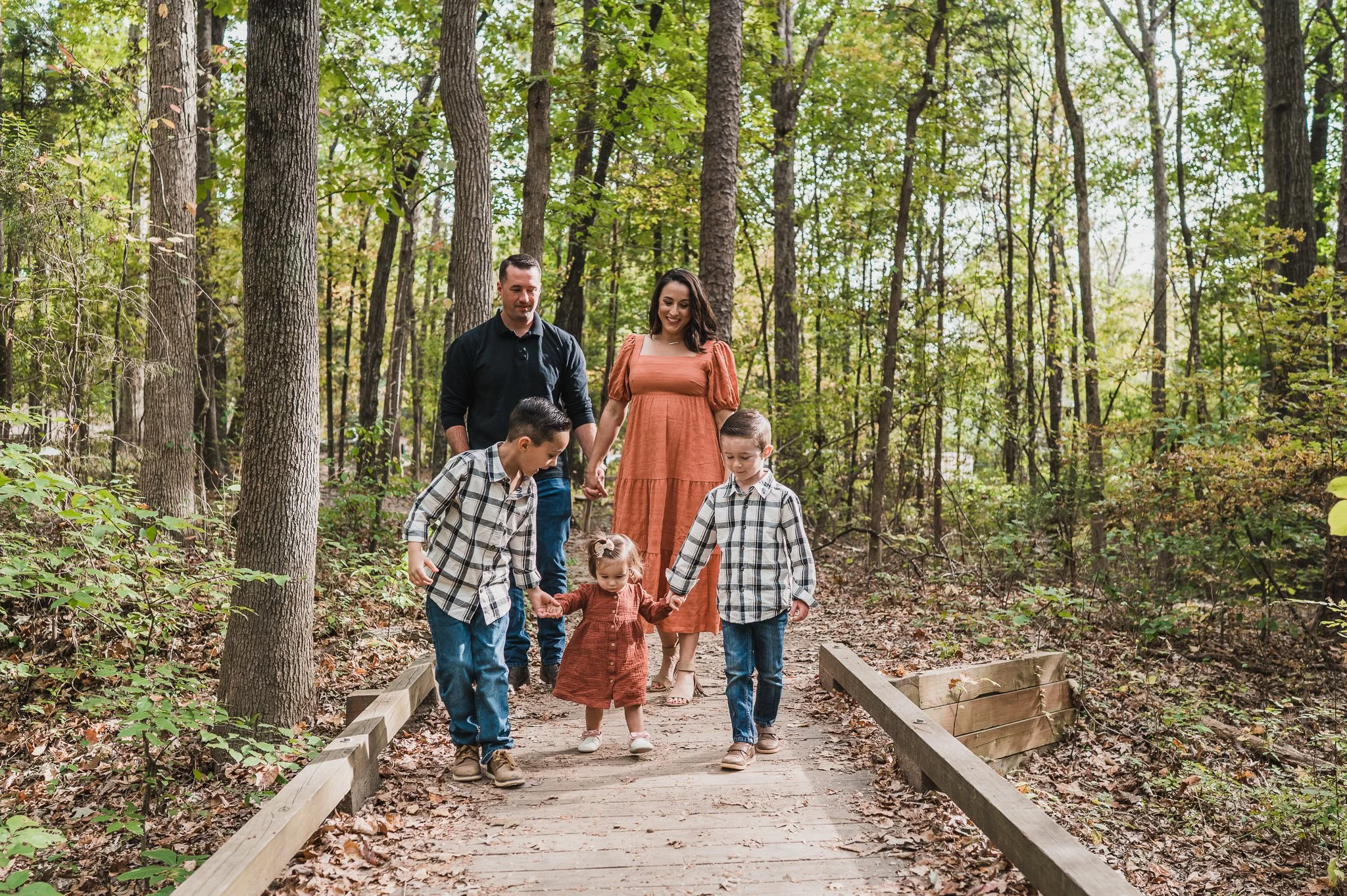 family in well coordinated outfits walking on bridge during fall family photo session at Big Rock Nature Preserve, Charlotte, NC