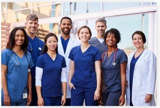 Group of diverse healthcare professionals in scrubs and lab coats standing outdoors.