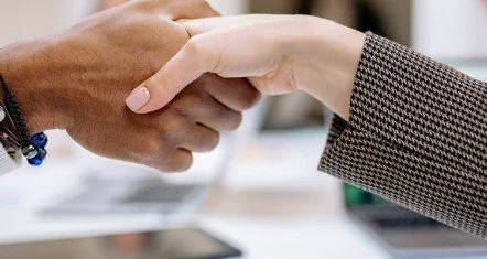 Two people shaking hands, one with darker skin and the other with lighter skin, in a professional setting.
