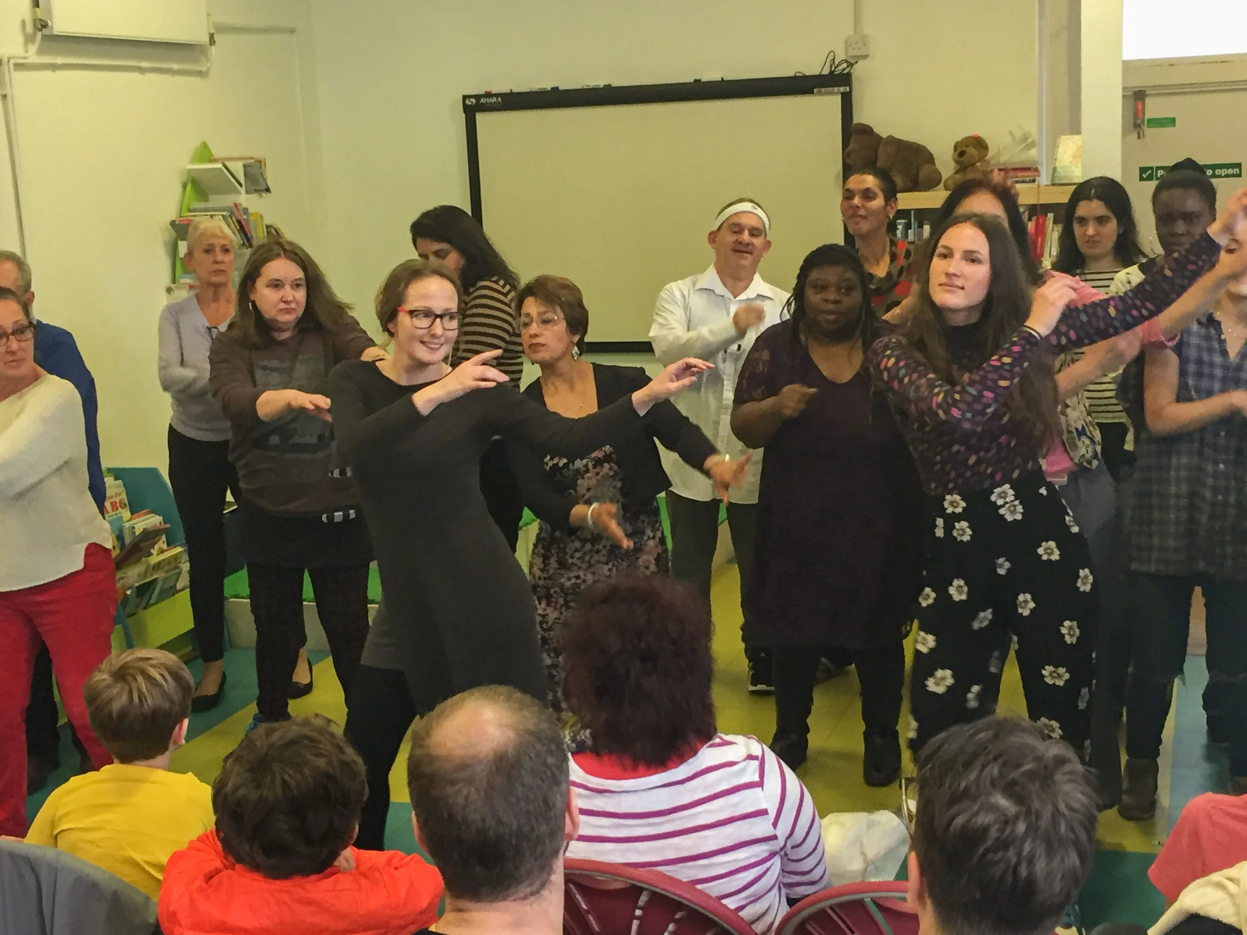 Group of women and children participating in a dance or celebration event in a colorful indoor space.