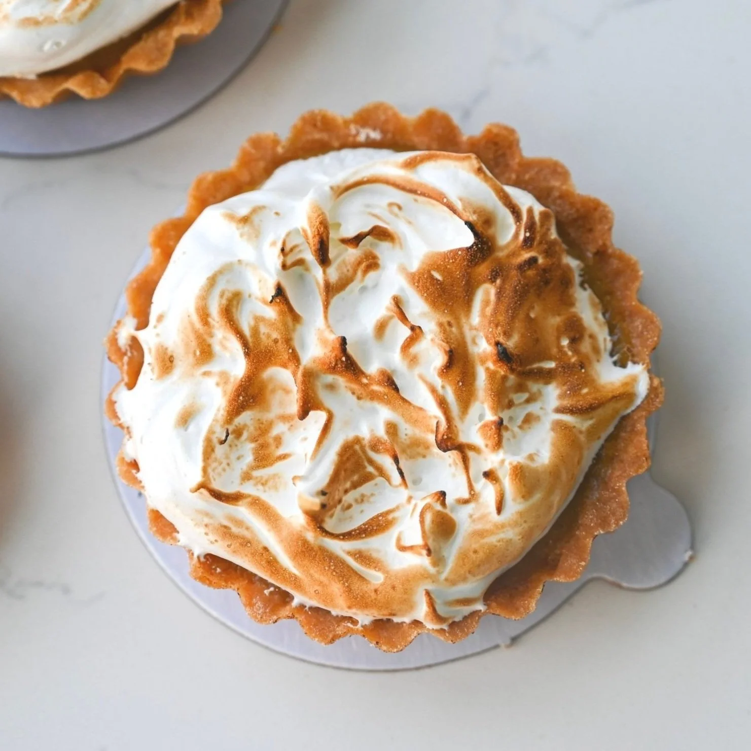 A lemon meringue tart with toasted meringue on a white surface.