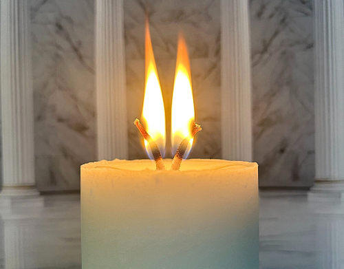 A candle with two flames burning in front of a marble background.