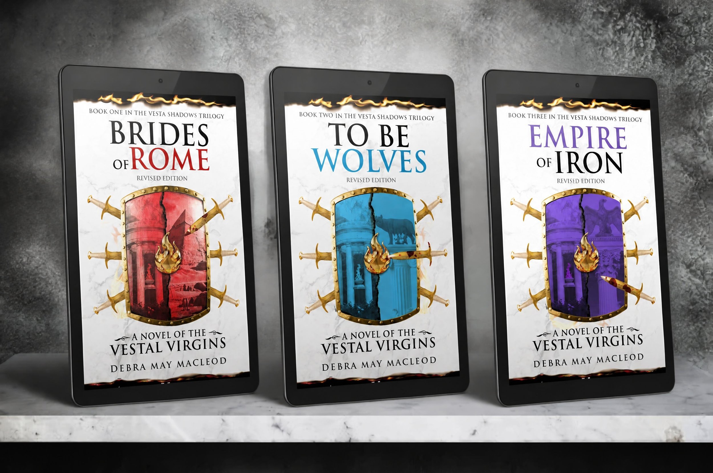 Three e-reader screens displaying book covers from the Vesta Shadows Trilogy. The covers feature a shield with swords and a flaming border at the top. The titles are 'Brides of Rome,' 'To Be Wolves,' and 'Empire of Iron,' with author Debra May MacLeod's name at the bottom.