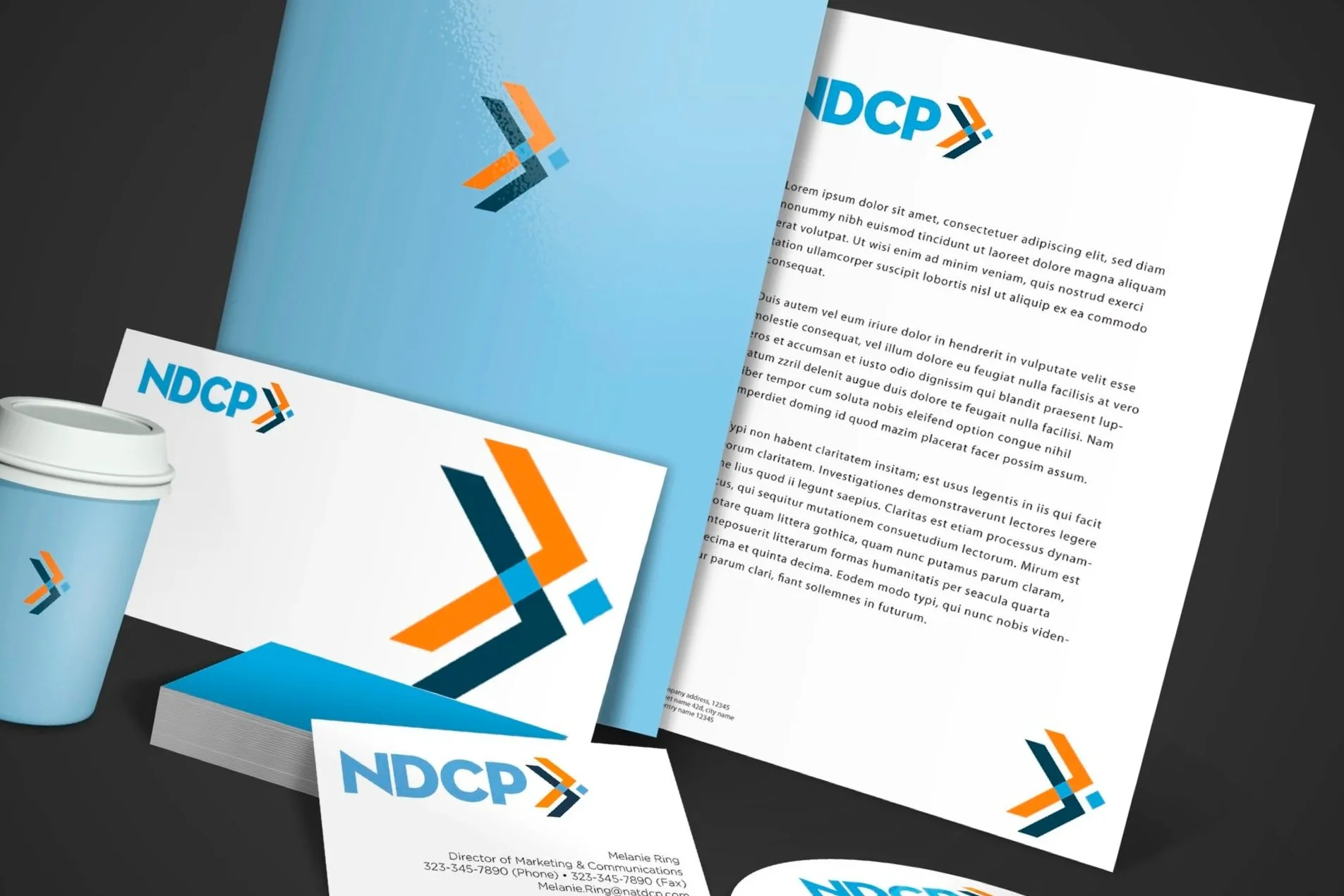Corporate branding materials including a folder, documents, business cards, a coffee cup, and a CD. All items feature a blue and orange logo with the acronym 'NDCP.'