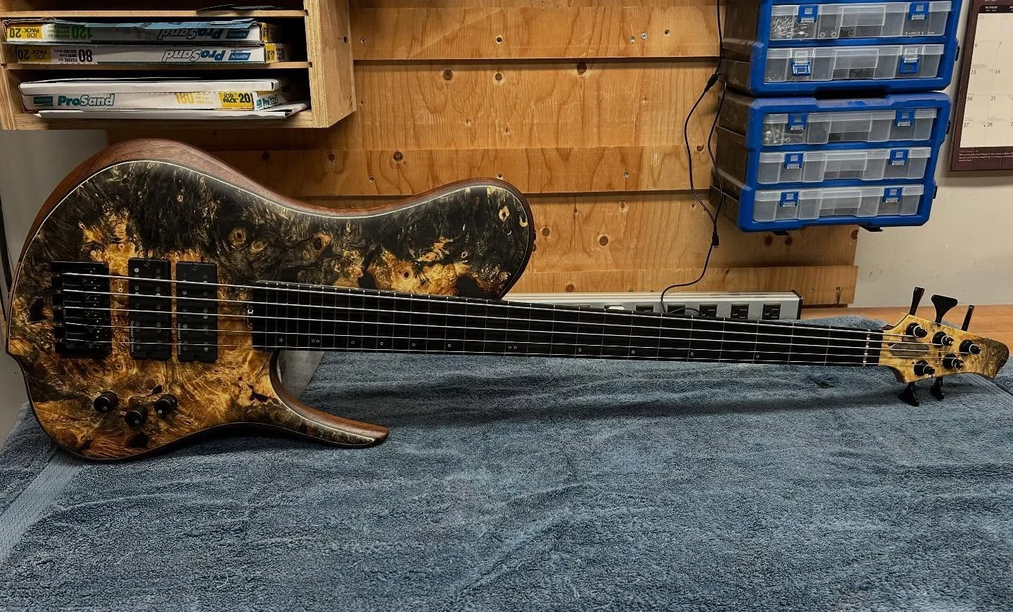 Bernie&rsquo;s 5-string Rhea is ready to ship!

Specs:
840 mm (33&rdquo;) scale length
16.5 mm bridge spacing, 45 mm nut
Buckeye Burl top
Black Walnut wings
3-piece White Oak neck
White Oak tone block
Purpleheart, Wenge, Flamed Maple accents
Gabon Eb