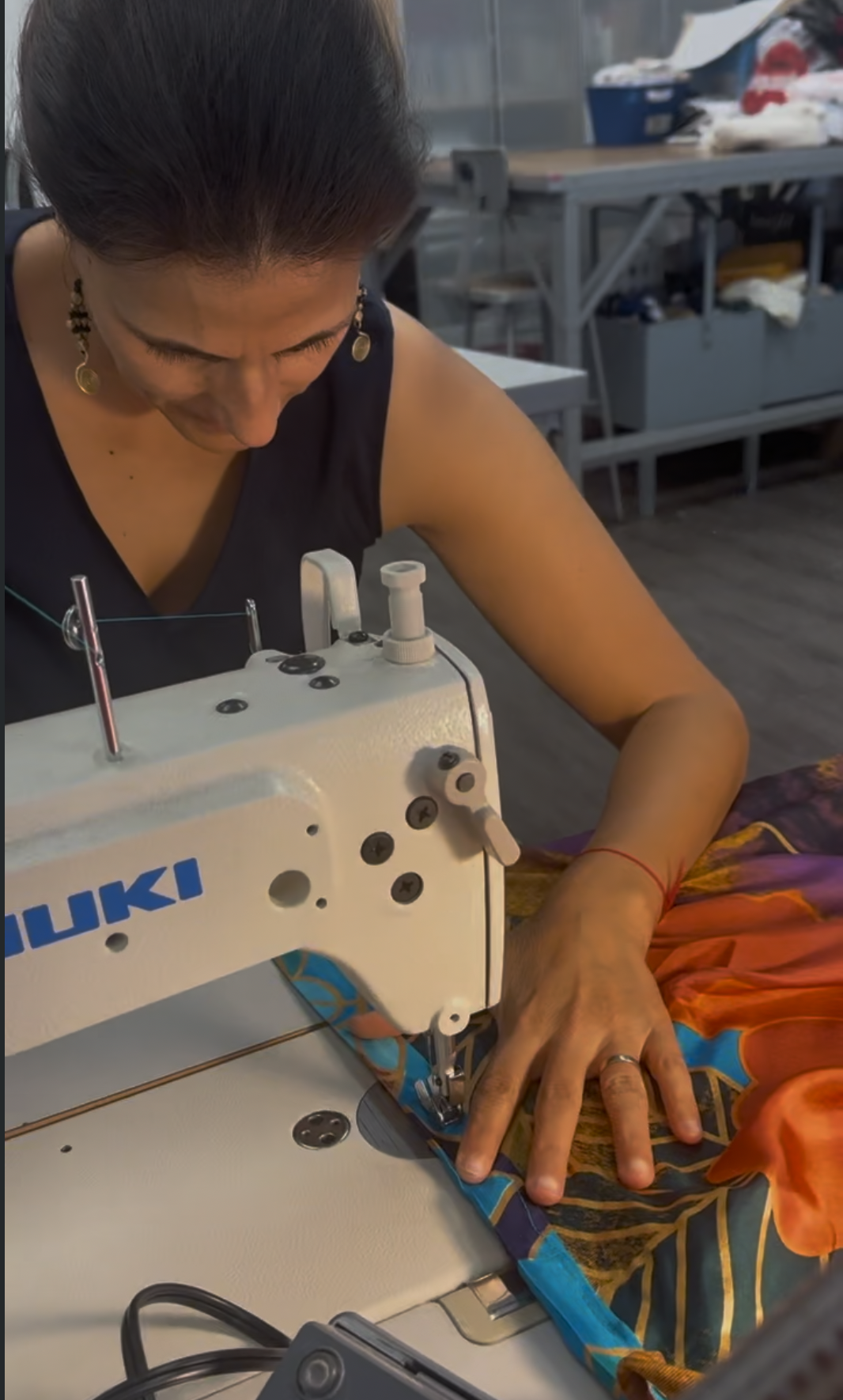 A woman sewing colorful fabric on a white sewing machine in a workspace.