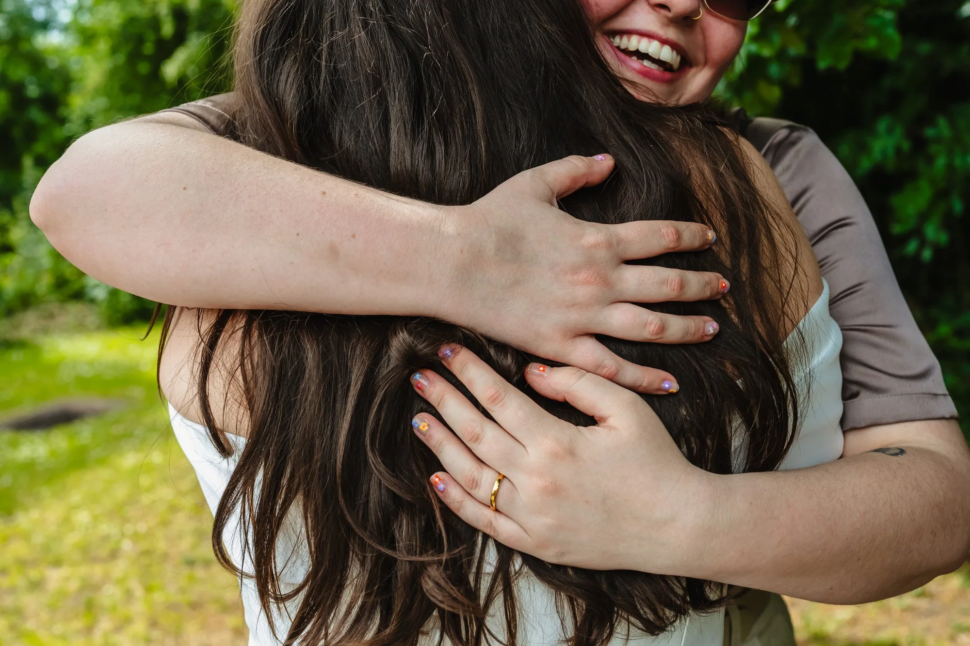 Two women hug on their wedding day in a relaxed portrait session. Only part of one woman's face is visible, and it shows a huge smile. Taken by documentary wedding photographer Caroline Goosey