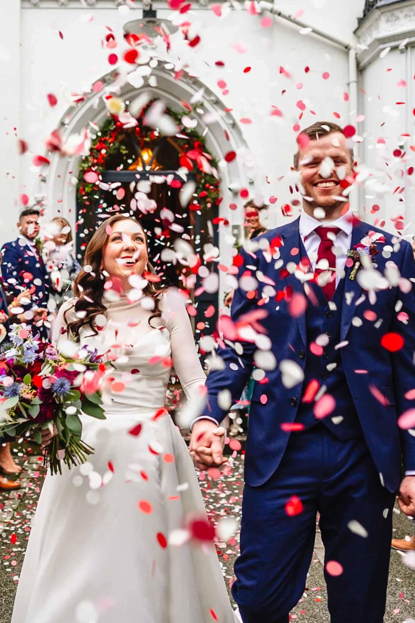 photograph of a just married couple exiting their wedding at Didsbury House Hotel to a shower of pink, white and red confetti