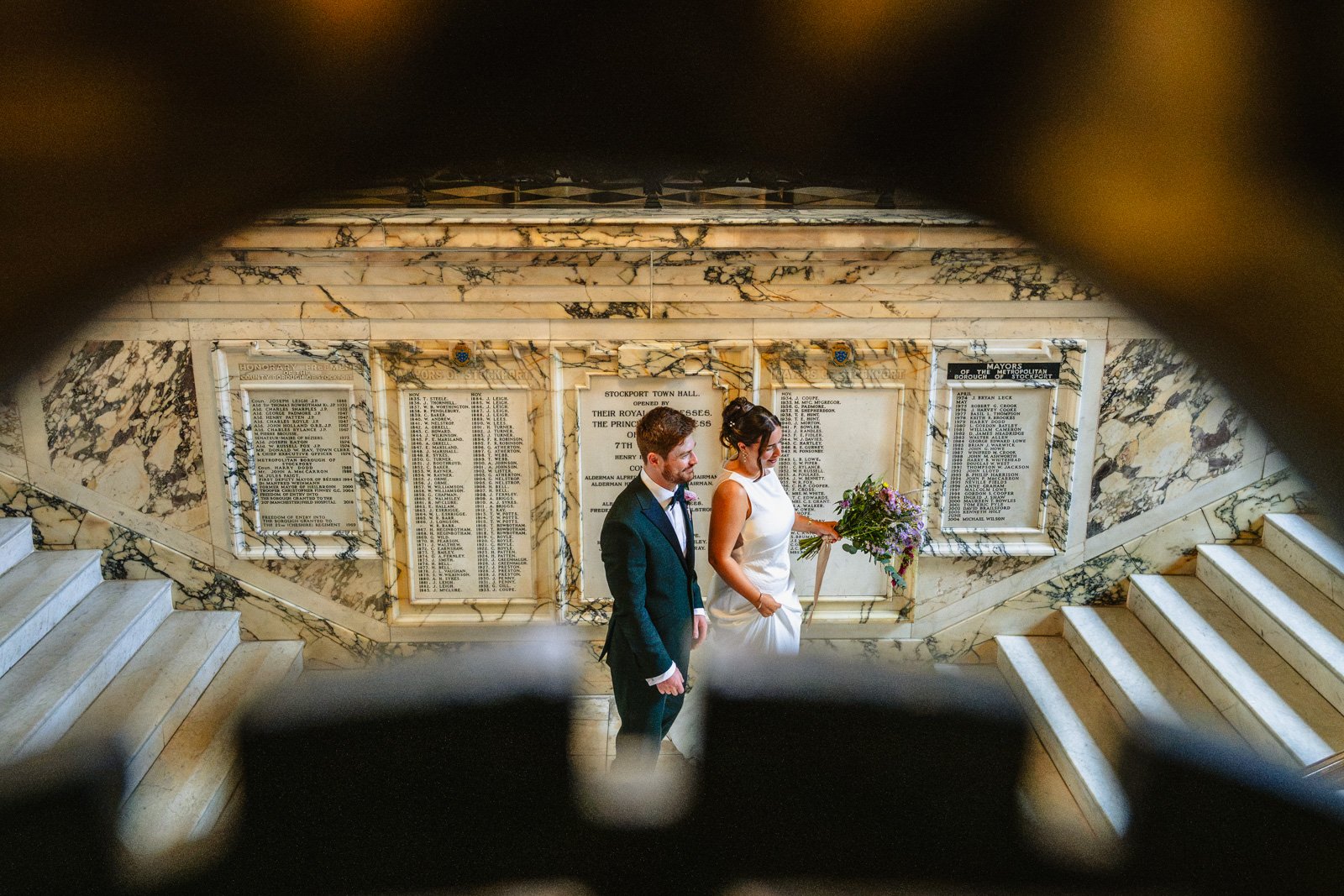 photograph of a bride and groom on a marble staircase, taken through iron railings.