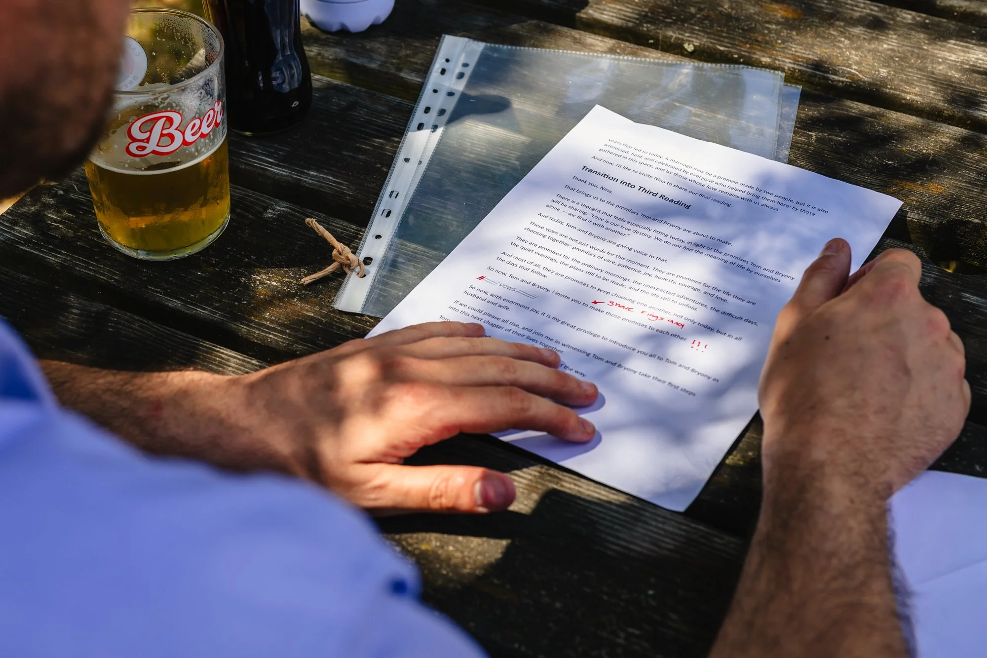 Photograph of a man’s hands on top of a piece of paper. The writing he’s reading is all about the wedding ceremony he’s about to perform for his friends. 