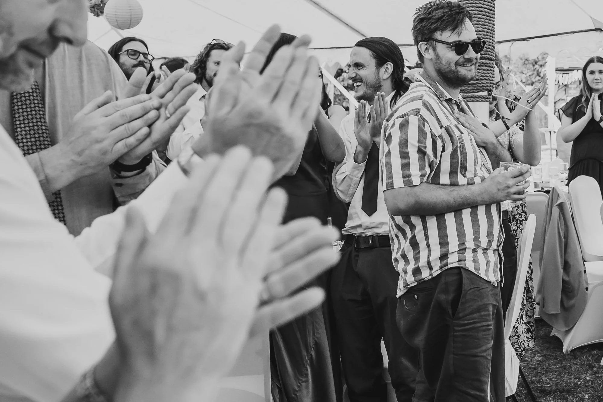  Black and white image of guests applauding. Clapping hands take up most of the frame, with smiling faces in the background. 