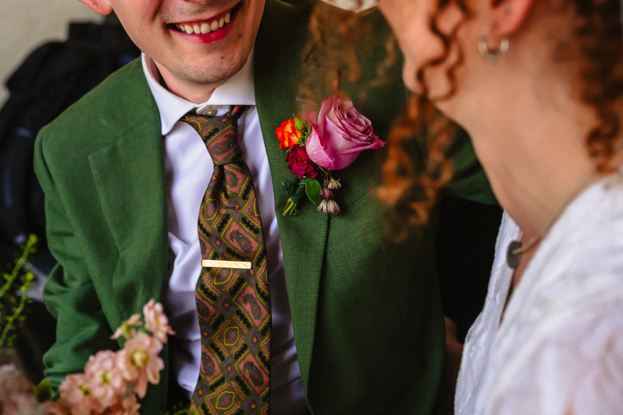  Close up photo of a couple looking at each other, with a focus on his tie and tie pin. His smile is visible. 