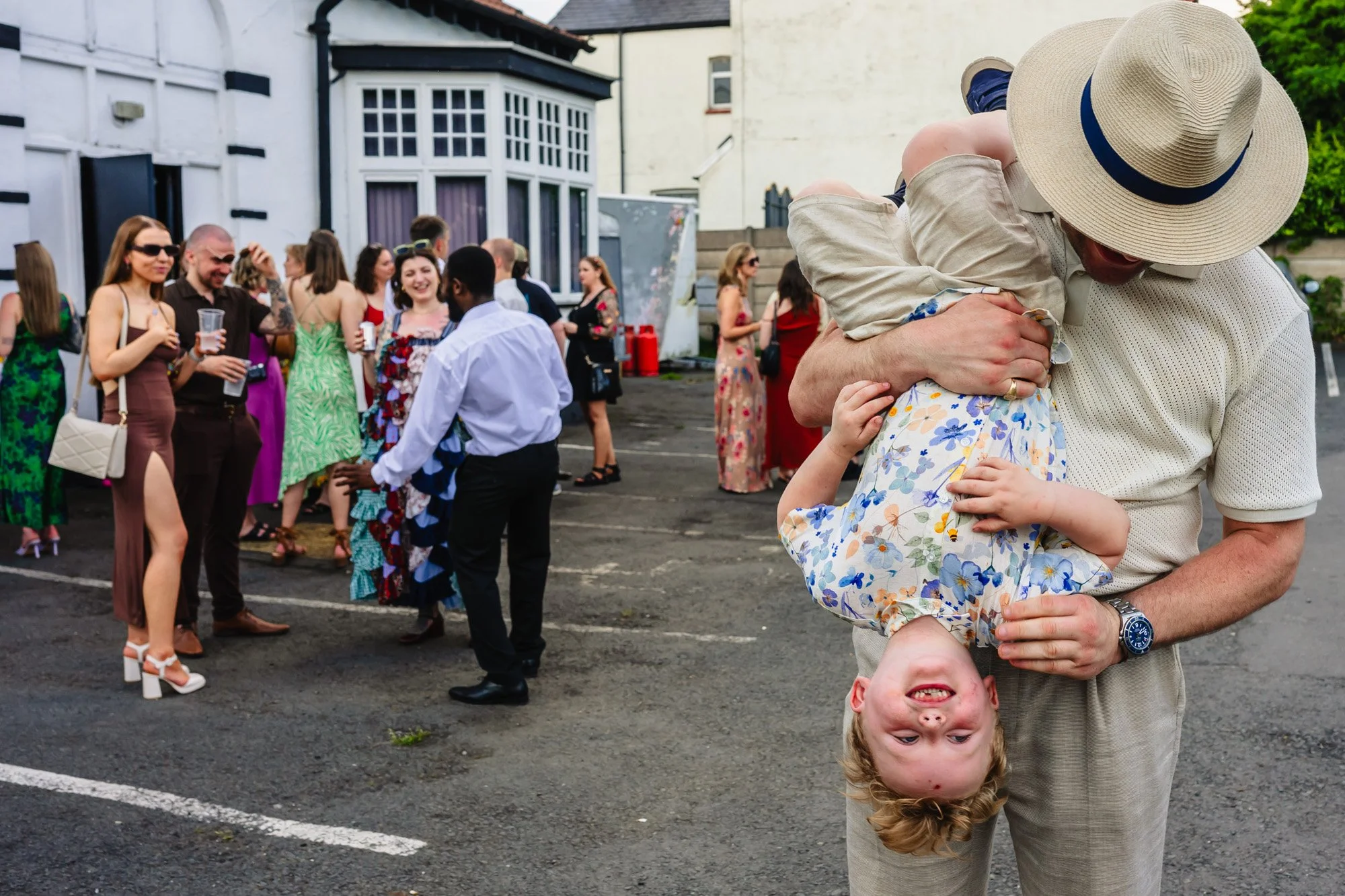  Photograph of a man holding a child upside down outside at a wedding reception in Manchester, by documentary wedding photographer Caroline Goosey 